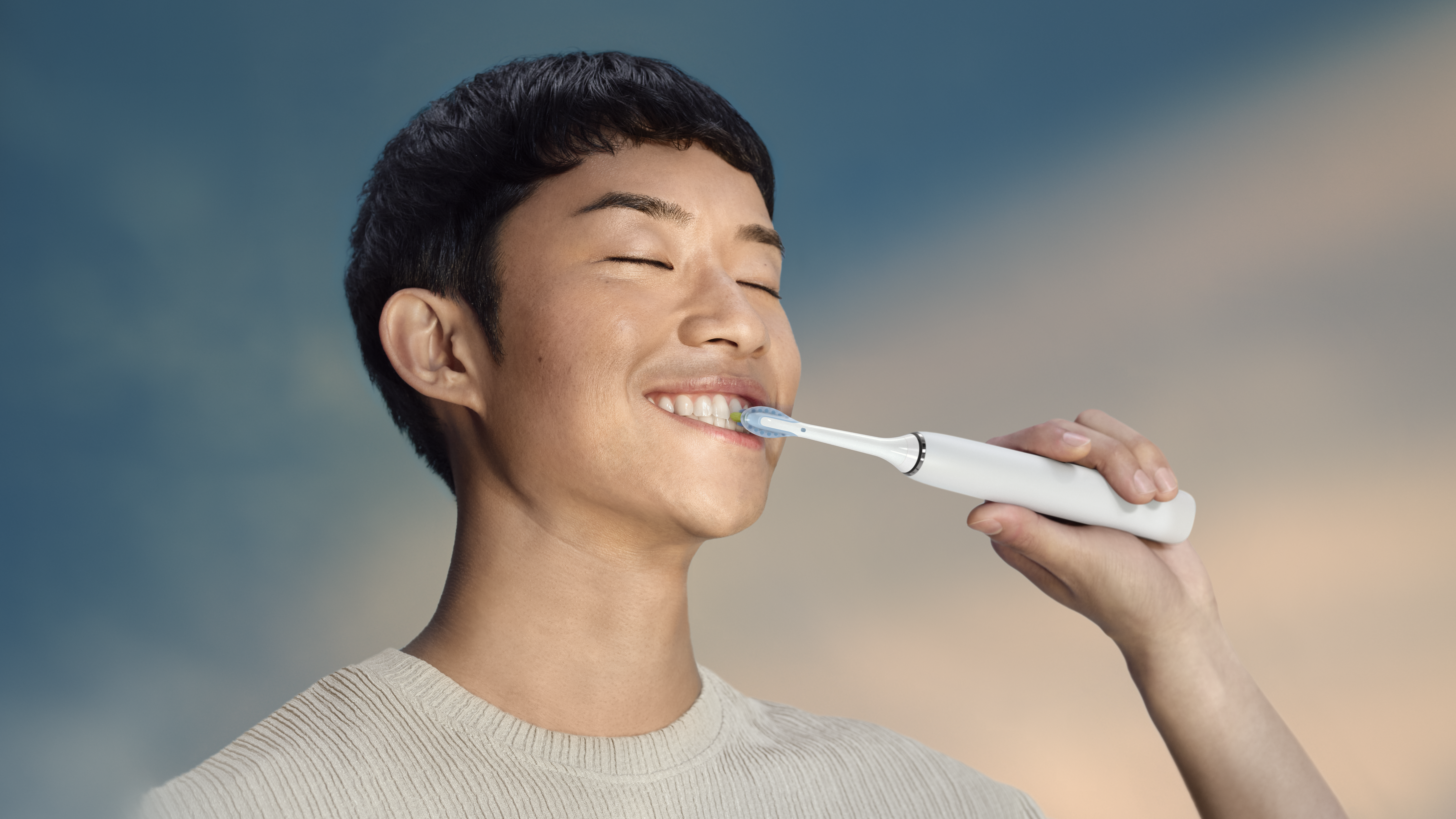 Un uomo si lava i denti con uno spazzolino elettrico. Sorride con gli occhi chiusi. Lo sfondo è blu e arancione.