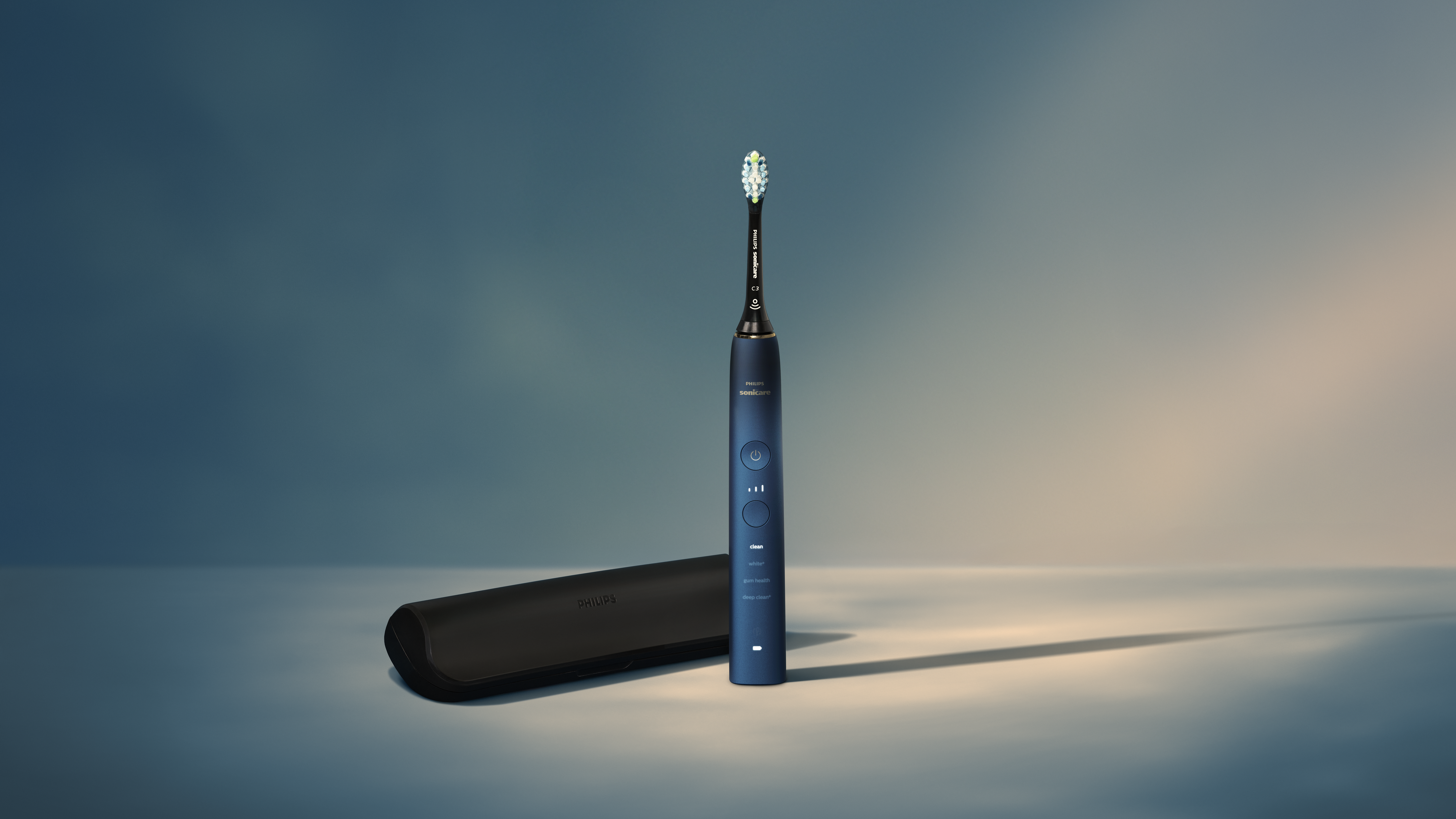 Uno spazzolino Philips Sonicare blu è in posizione verticale. Un astuccio nero è a sinistra. Lo sfondo è sfumato blu e beige.