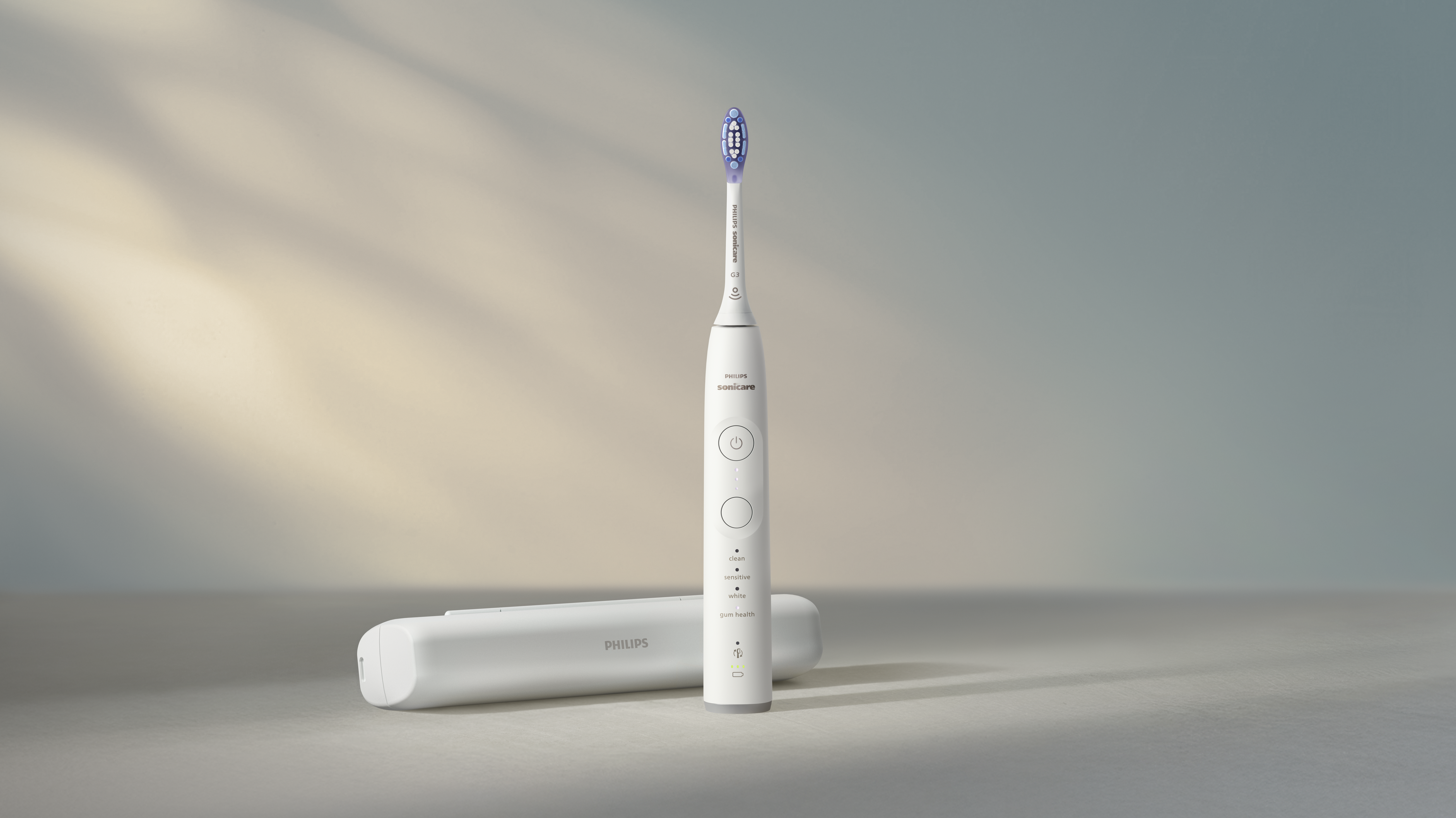 Une brosse à dents électrique Philips Sonicare blanche et un étui de chargement sont sur une surface gris clair, avec un fond dégradé bleu clair et beige.