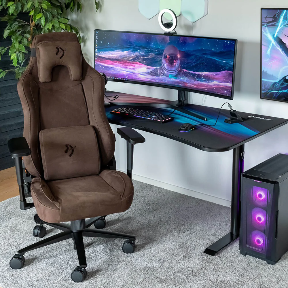 Egy barna gamer szék egy asztal mellett, melyen egy űrhajóst ábrázoló monitor van. Jobbra egy számítógép torony.