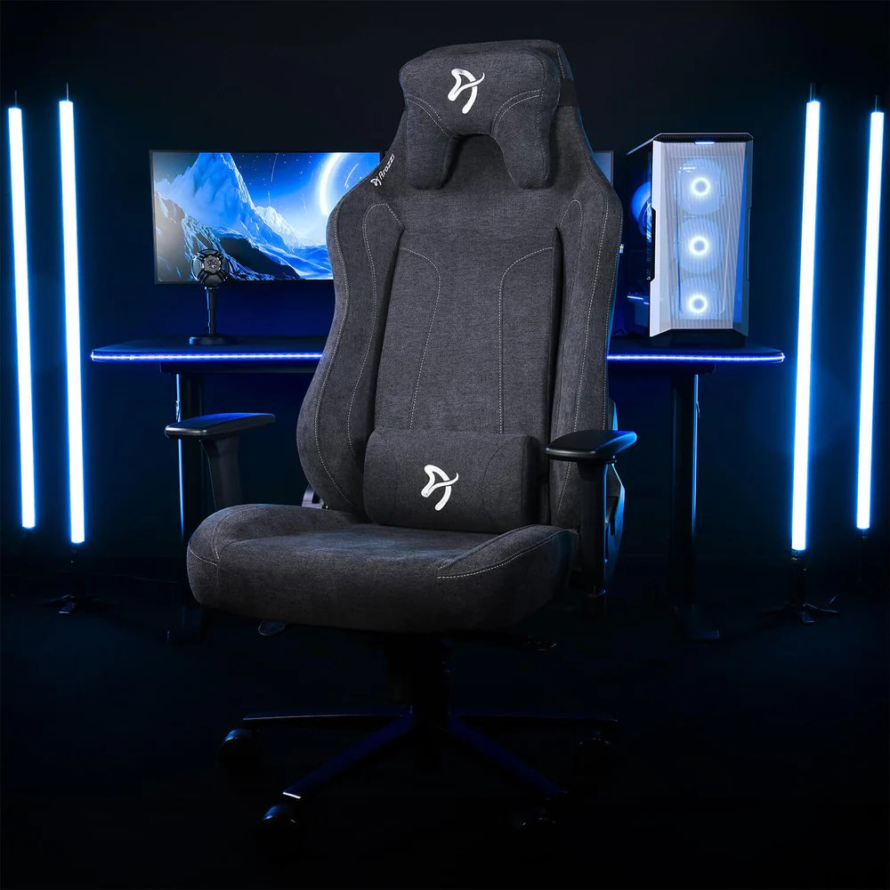Egy szürke gamer szék egy asztal előtt, PC-vel és monitorral. Kék fények világítják meg a jelenetet, modern megjelenést kölcsönözve.