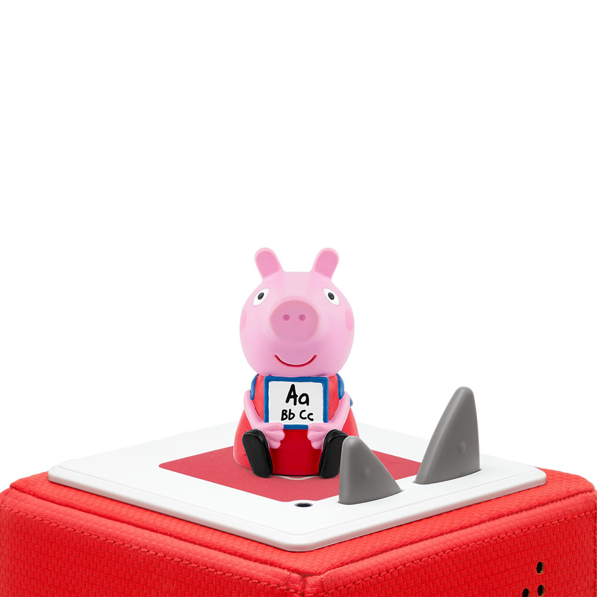 Rosa Peppa Wutz-Figur mit einem Schild mit der Aufschrift 'Aa Bb Cc' sitzt auf einem roten Block mit grauen Haifischflossen.