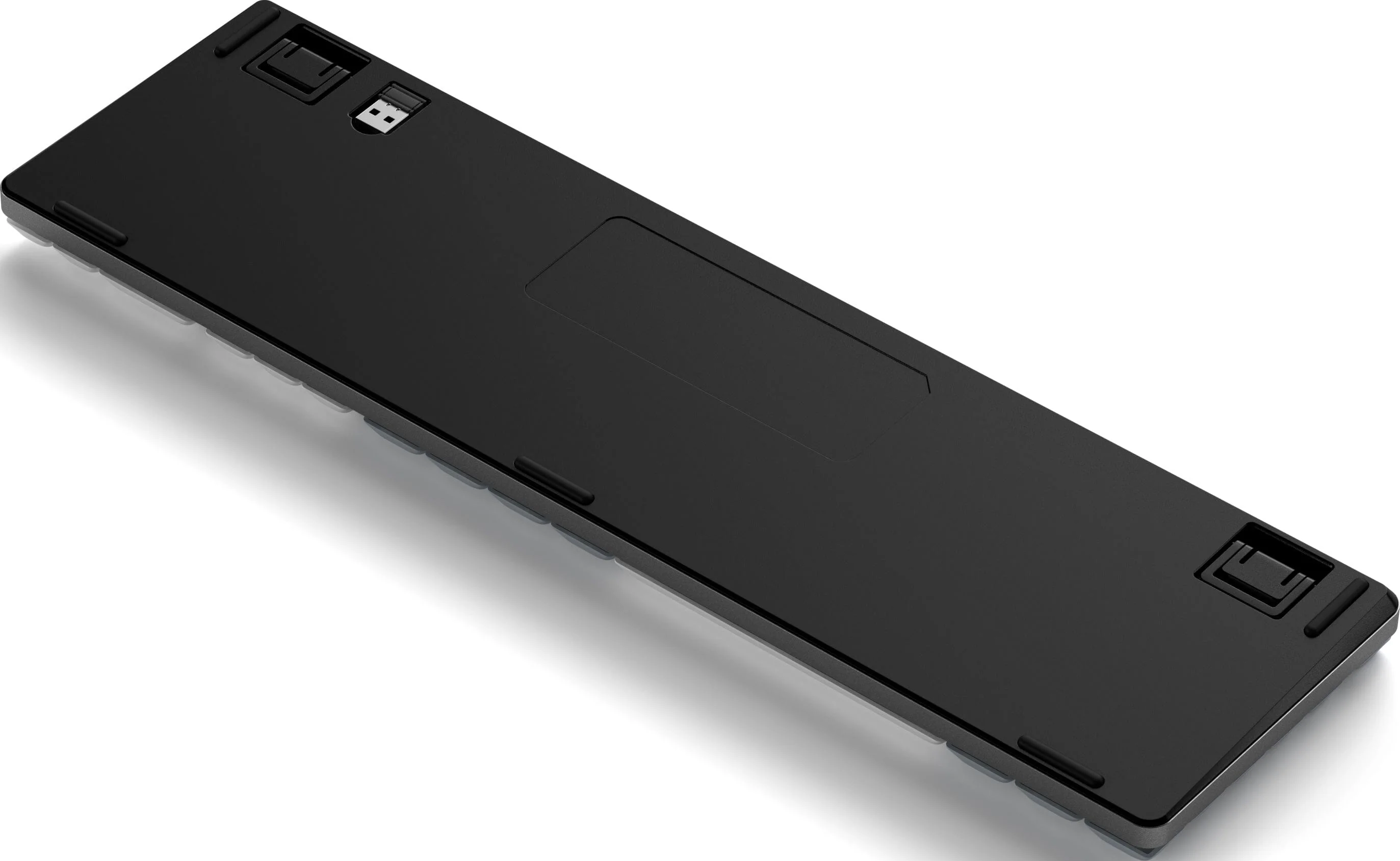 Die Unterseite einer schwarzen Tastatur. Sie hat einen USB-Anschluss, Gummifüße und eine Aussparung für eine Batterie.