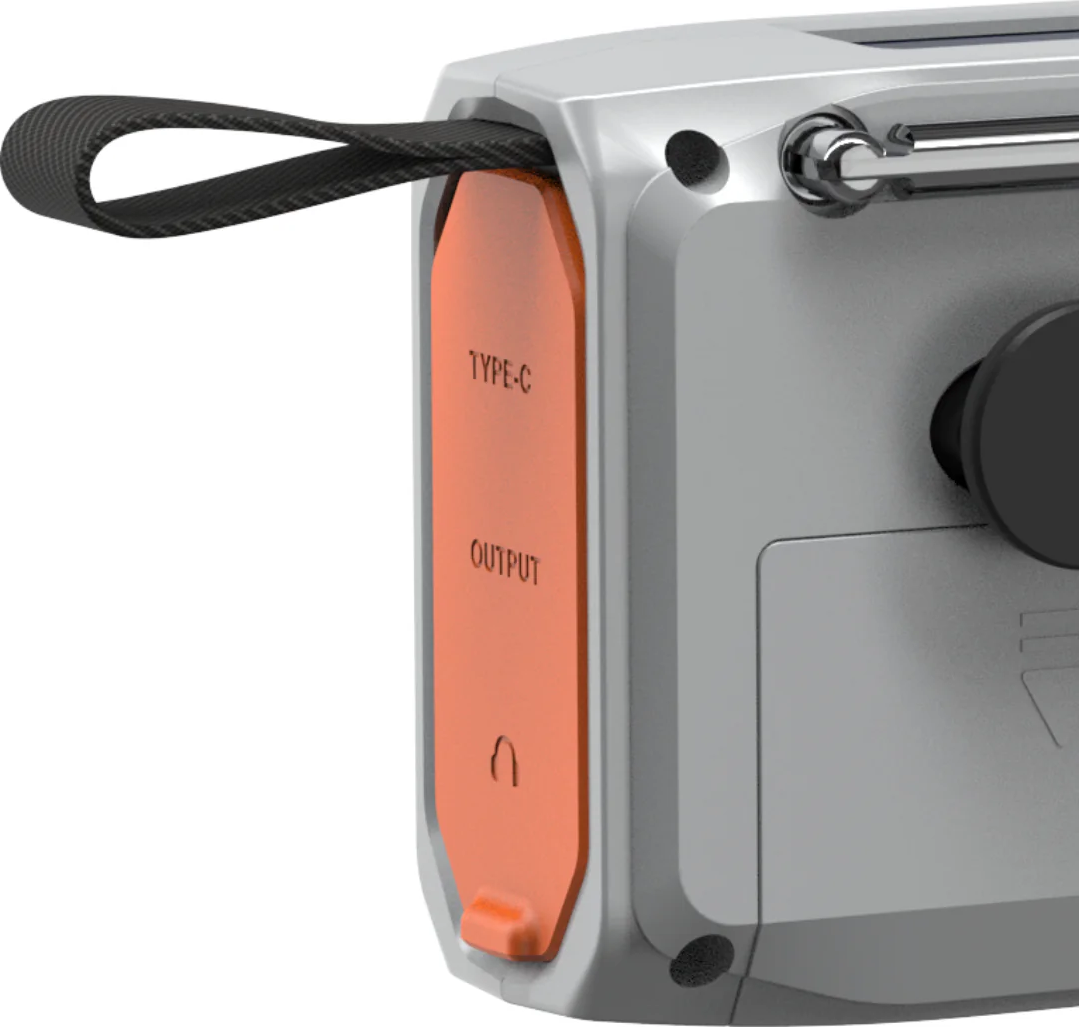 Gros plan d'un appareil gris argenté avec un couvercle de port orange étiqueté 'TYPE-C OUTPUT'. Une sangle noire est attachée.