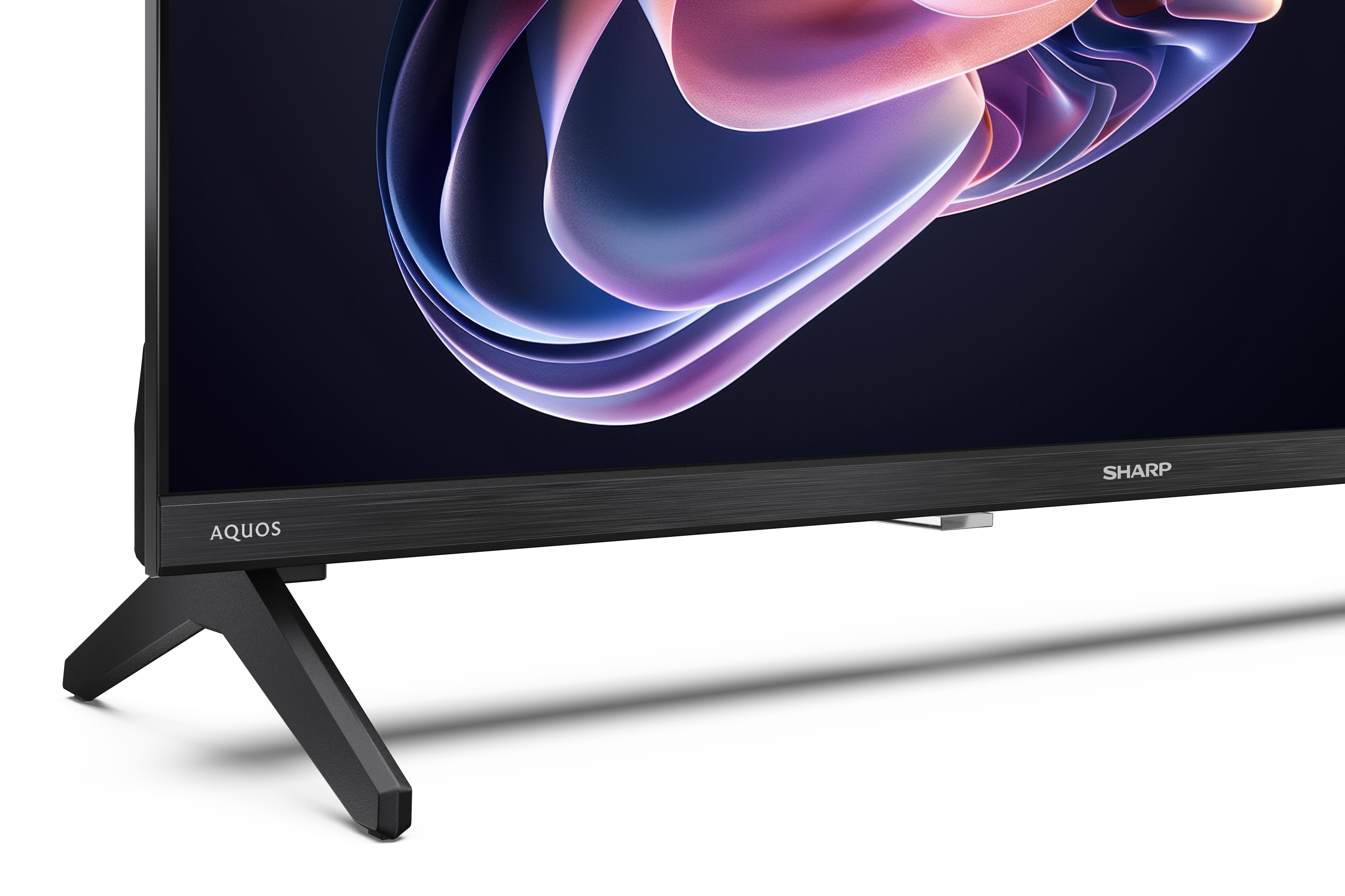 Egy Sharp Aquos TV látható. A képernyő színes absztrakt képet jelenít meg. A TV fekete lábakkal és fekete kerettel rendelkezik.