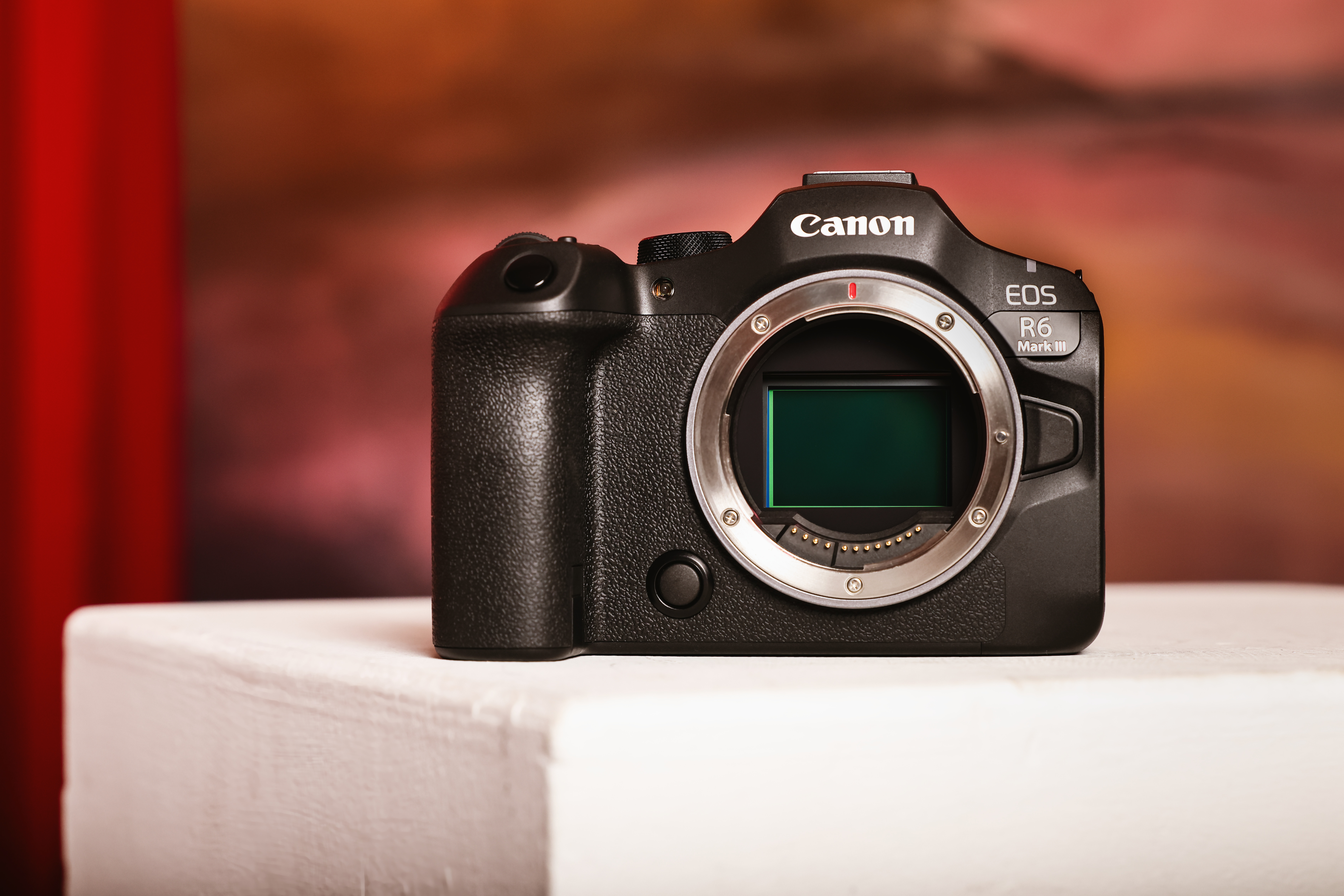 Eine schwarze Canon EOS R6 Mark III Kamera liegt auf einer weißen Oberfläche. Der Hintergrund ist verschwommen.