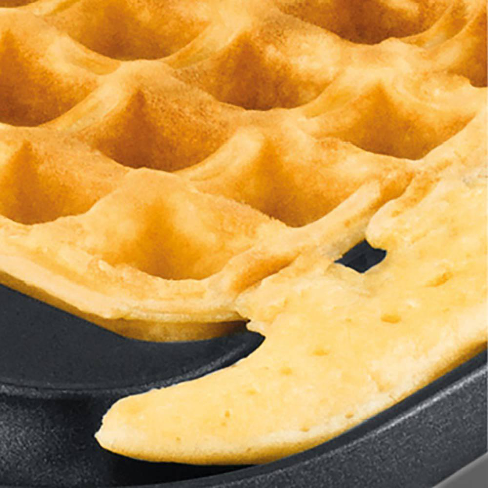 Nahaufnahme einer Waffel. Goldbraune, gebackene Waffel mit abgebrochenem Stück, das das weiche Innere zeigt, auf schwarzem Untergrund.