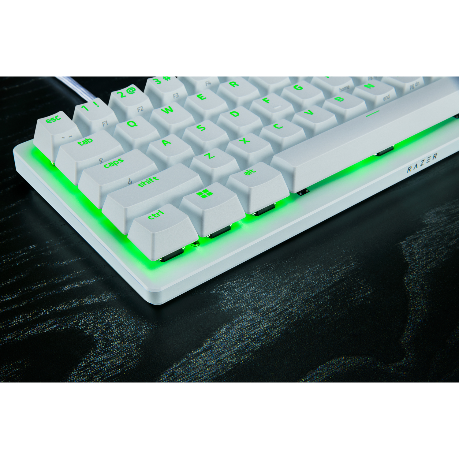 A white Razer keyboard with green illuminated keys. The keyboard sits on a dark wooden surface. The Razer logo is visible.