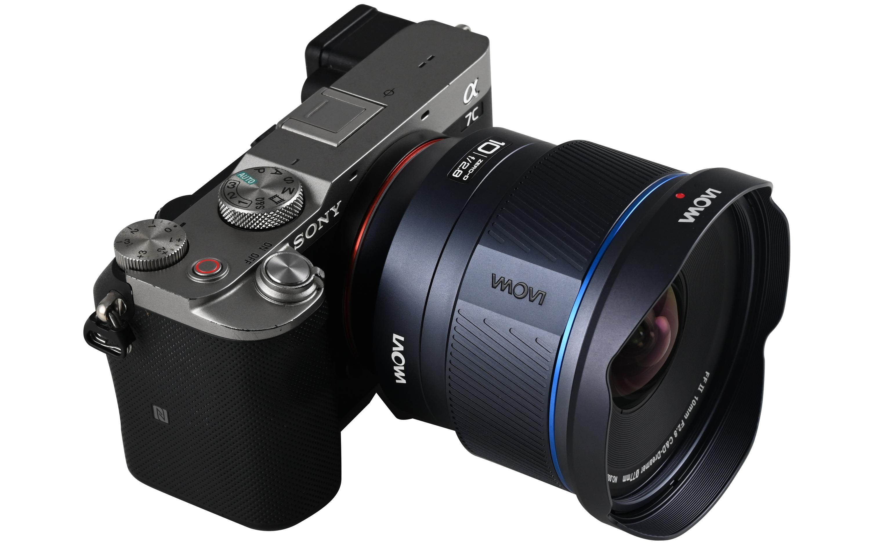 Eine silberne Sony-Kamera mit schwarzem Objektiv auf weißer Oberfläche. Das Objektiv hat einen blauen Ring und eine schwarze Gegenlichtblende.