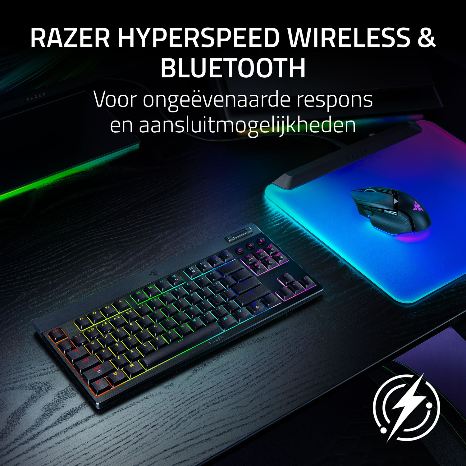 A black keyboard with colorful keys and a mouse on a glowing blue pad on a wooden table. Razer branding is visible.