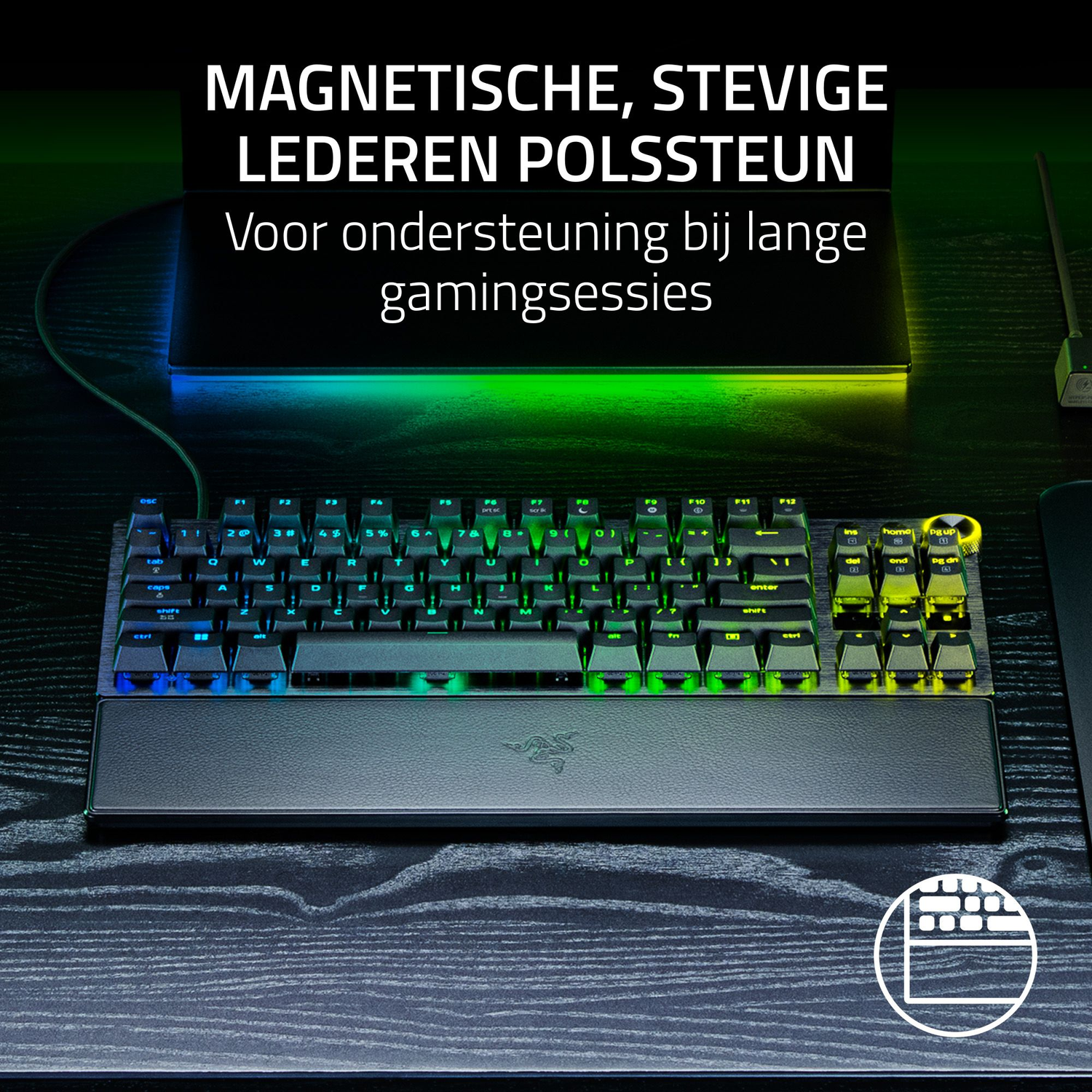 A black keyboard with a wrist rest on a wooden desk. The keyboard has green and blue lights.
