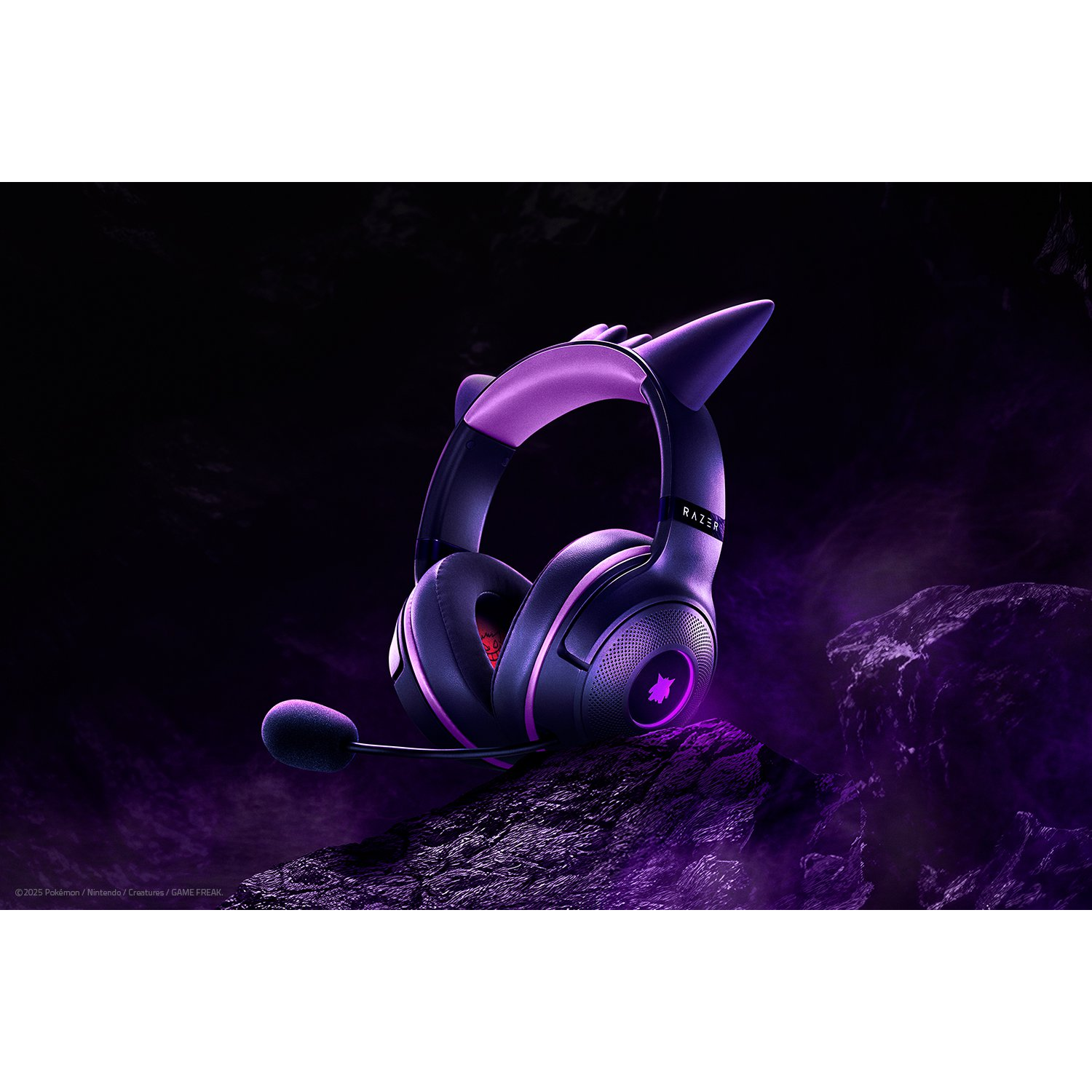 Een Razer-headset, zwart en paars, ligt op een rots. Het heeft kattenoren, een microfoon en een oplichtend logo.