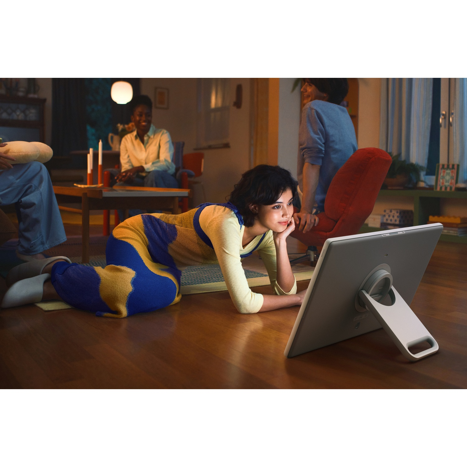 Femme au sol regardant une tablette. Personnes en arrière-plan. Bougies sur la table. Chaise rouge. Intérieur cosy.
