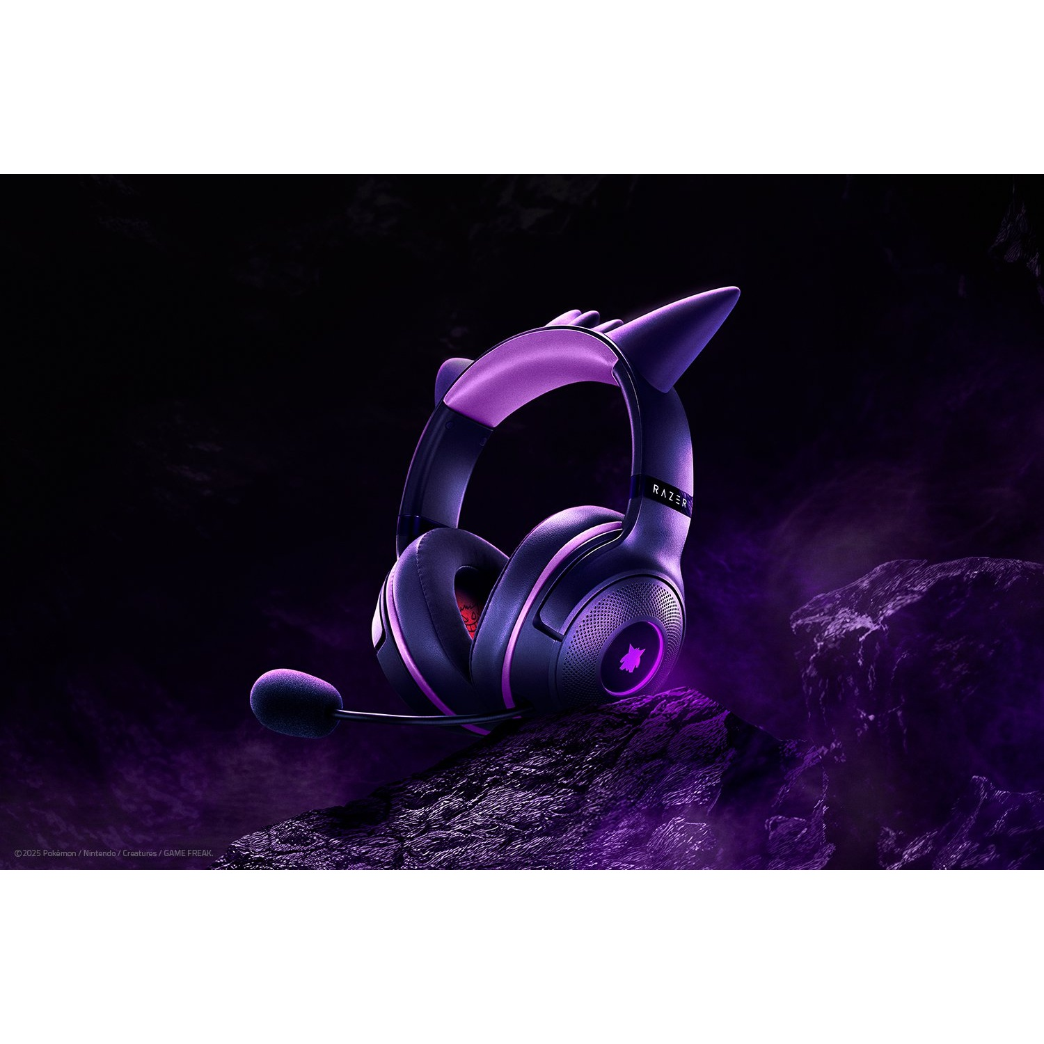 A purple gaming headset with cat ears sits on a rocky surface, with a dark, smoky background. The Razer logo is visible.