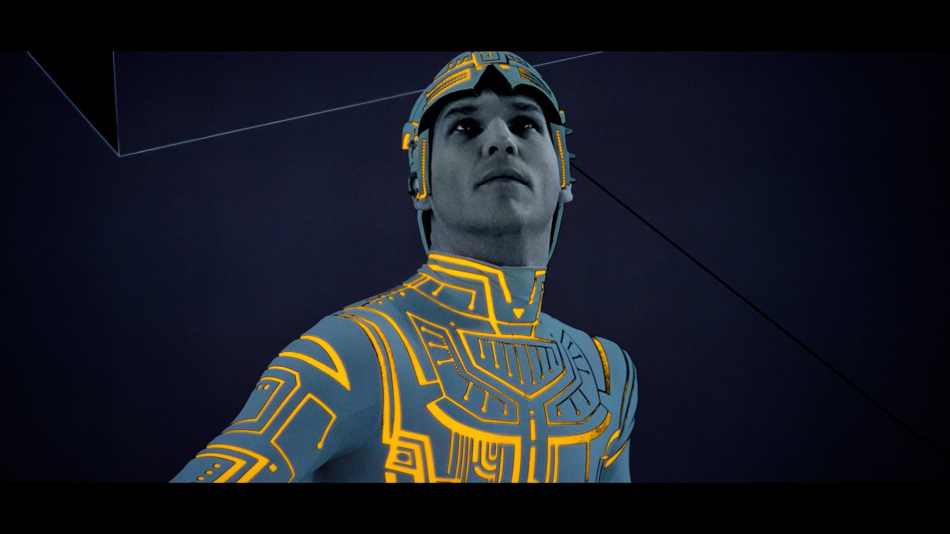 Ein Mann in einem futuristischen Anzug mit gelb leuchtenden Linien. Er schaut nach oben. Dunkelblauer Hintergrund mit geometrischen Formen.