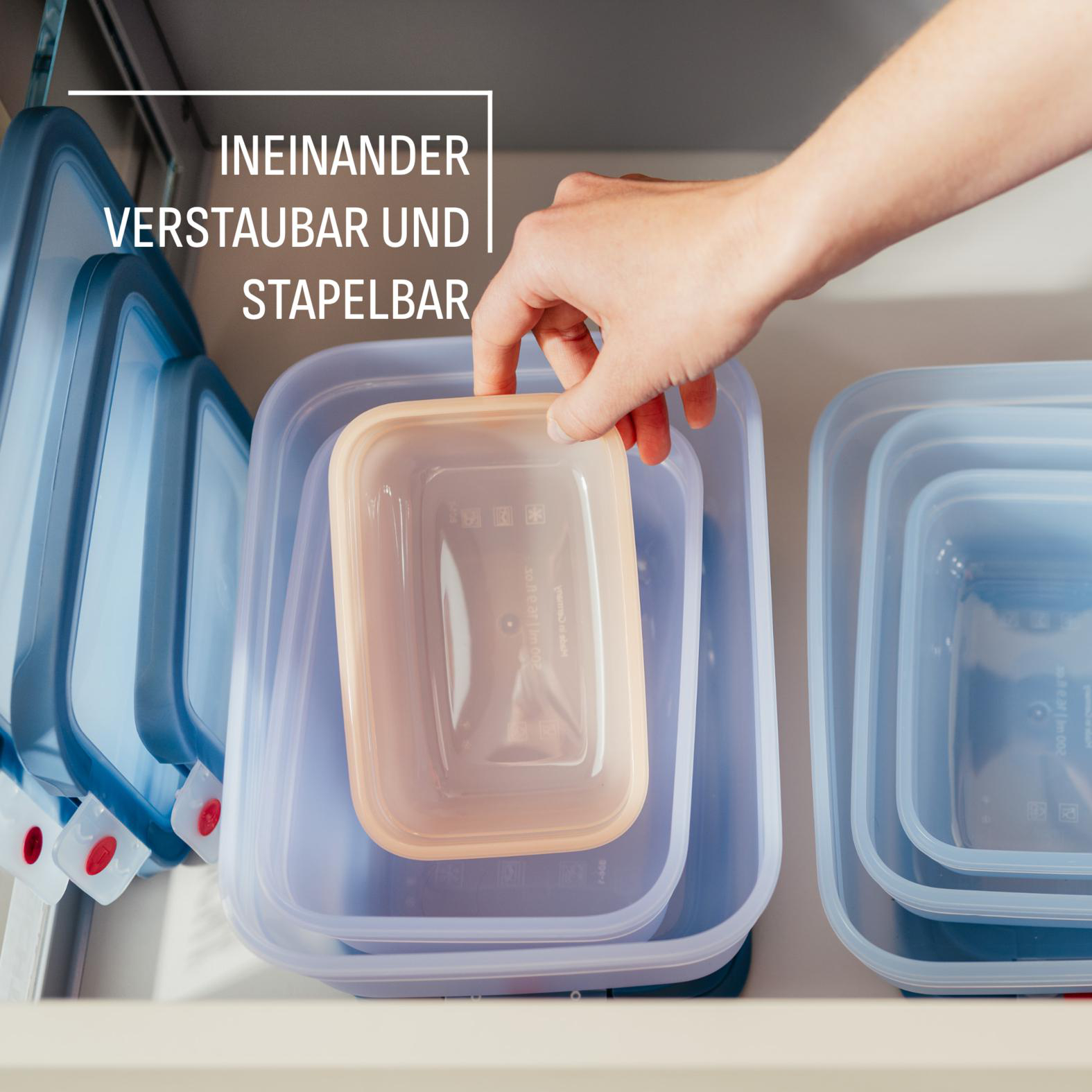 Hand legt einen beigefarbenen Behälter in einen Stapel blauer und transparenter Lebensmittelbehälter in eine Schublade.