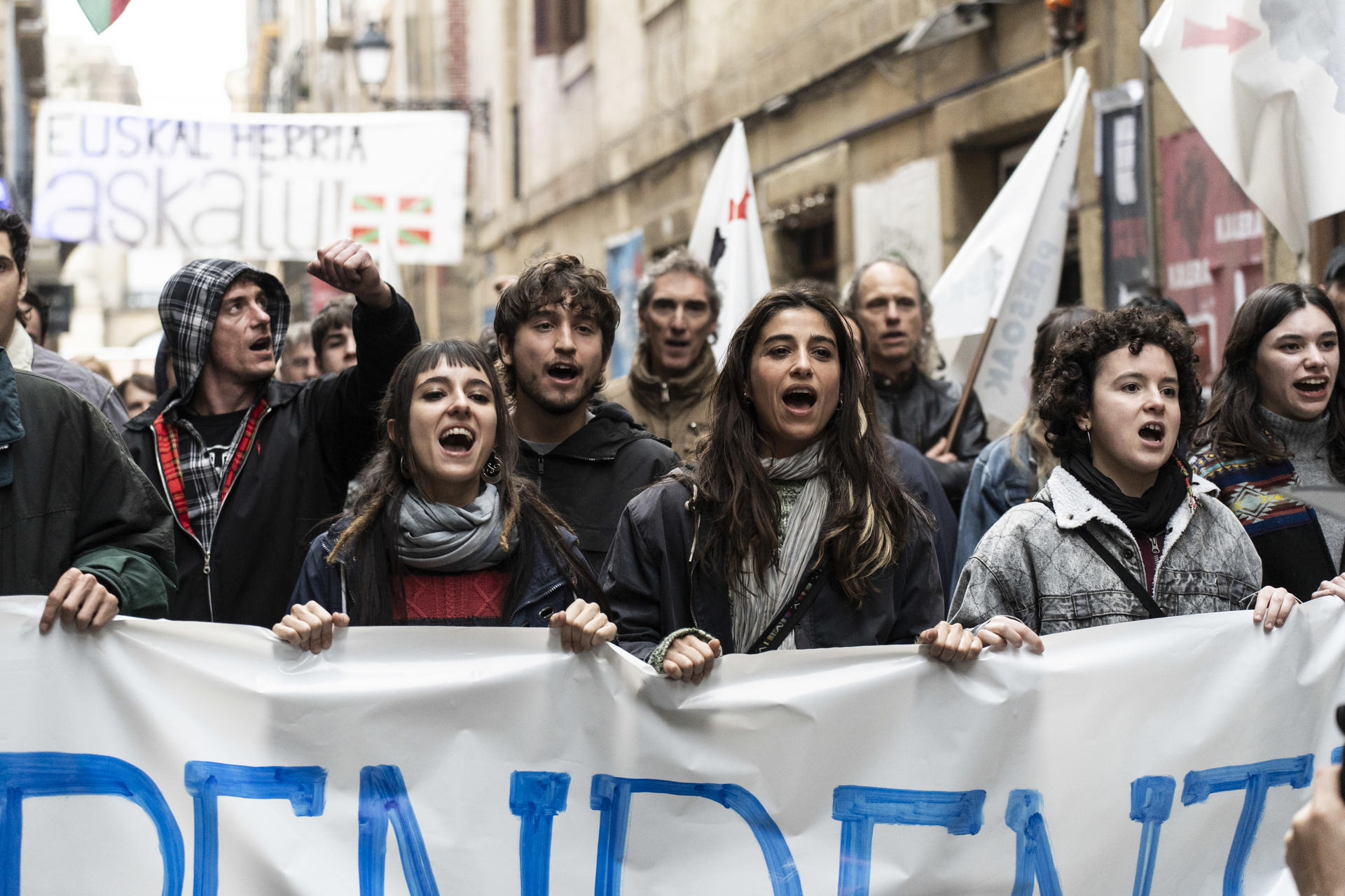 Eine Menge protestierender Menschen hält ein Banner. Einige schreien. Ein Schild mit der Aufschrift 'Euskal Herria askatu' ist sichtbar.