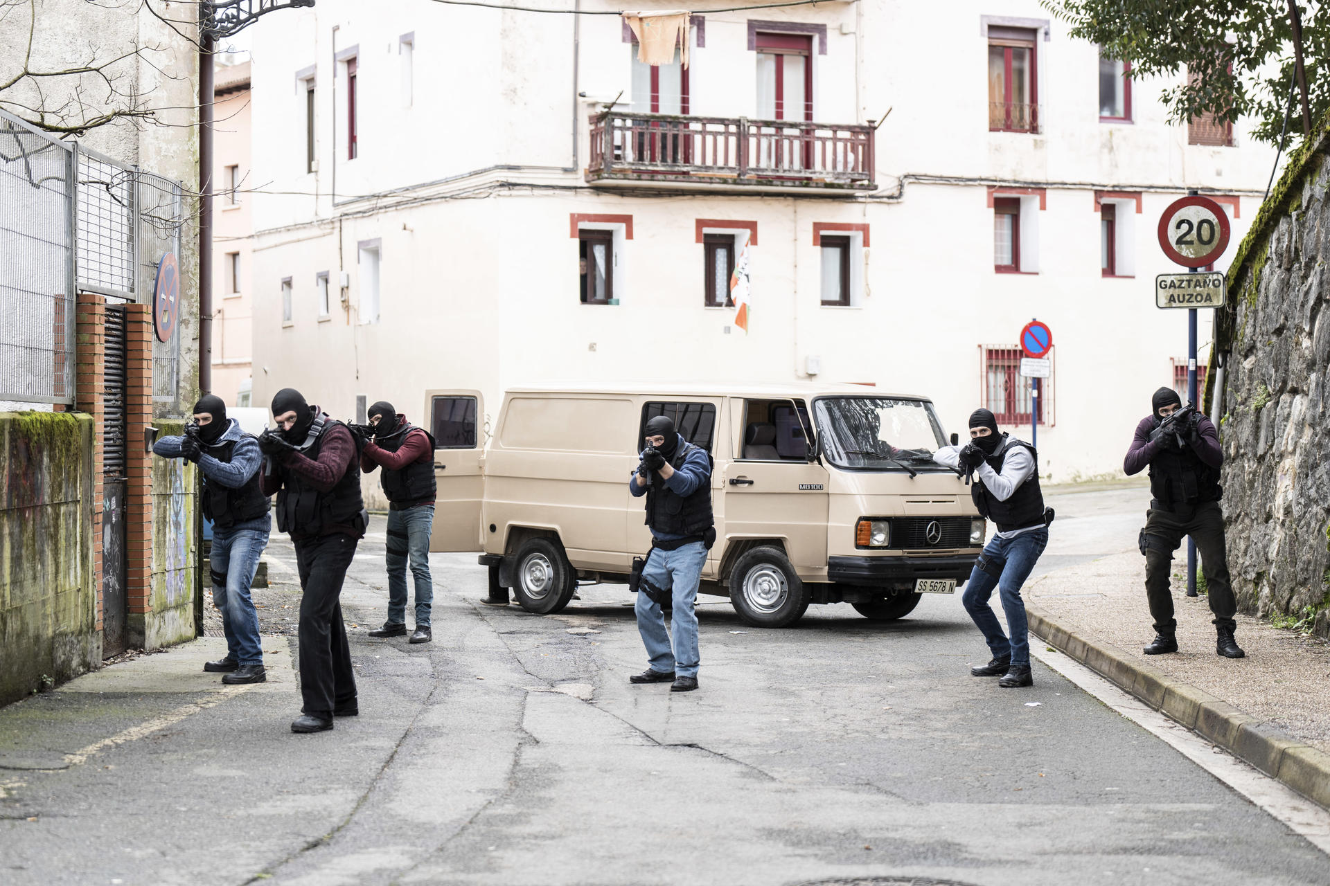 Bewaffnete Personen in taktischer Ausrüstung zielen mit Waffen in der Nähe eines Transporters und Gebäudes. Szene deutet auf eine Polizei- oder Militäroperation hin.