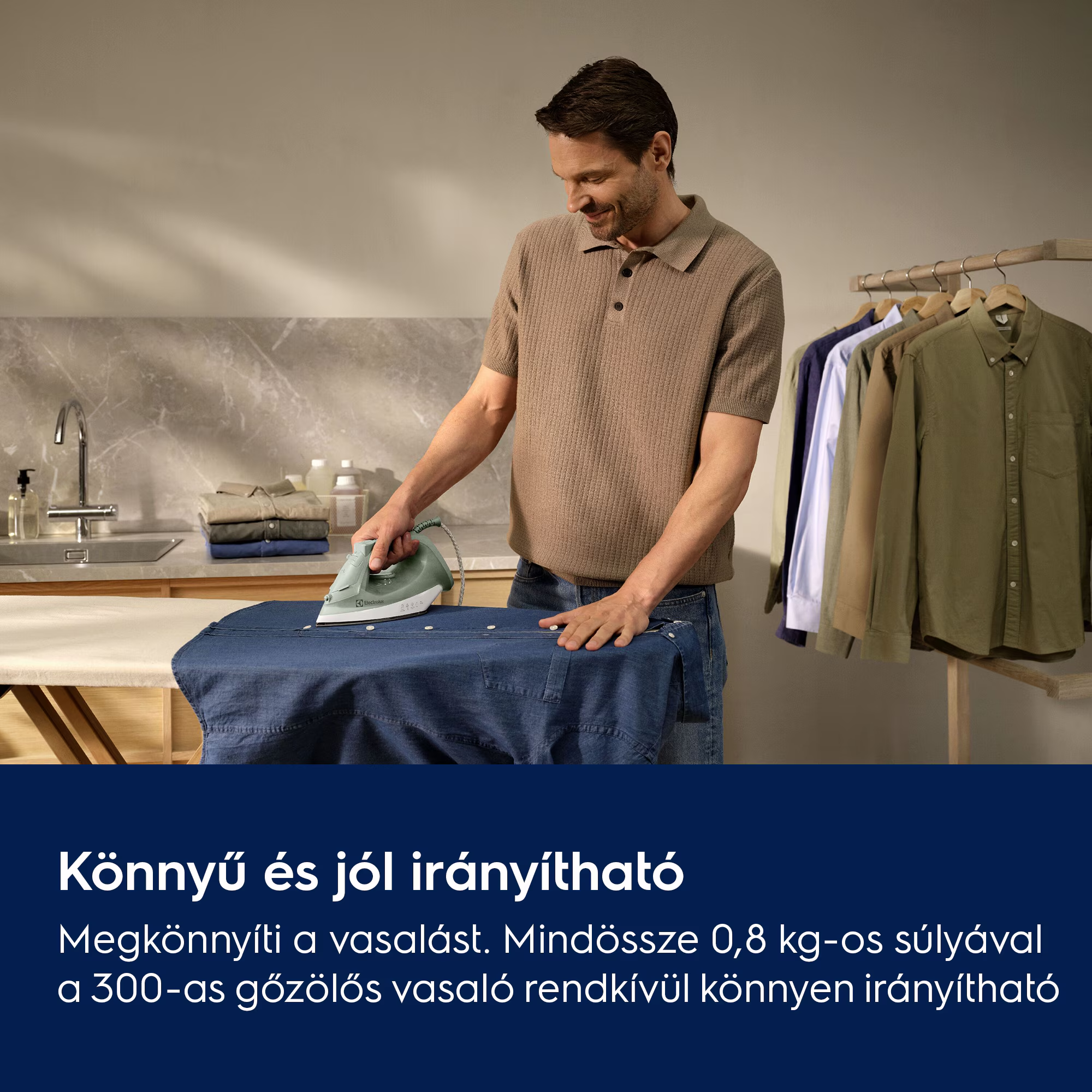 Egy férfi kék inget vasal. Ingek lógnak egy állványon. Egy halom összehajtott ing a pulton van.