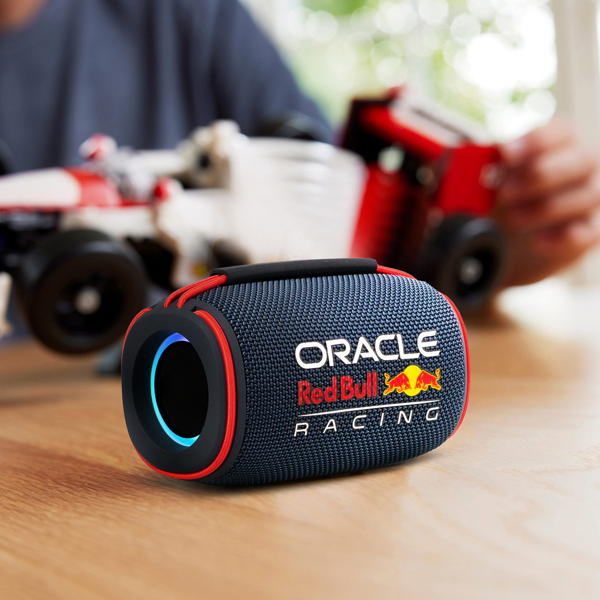 Un haut-parleur bleu et noir avec le logo Oracle Red Bull Racing. Une voiture jouet est à l'arrière-plan.