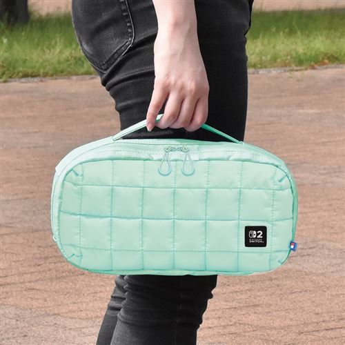 Una persona sostiene una bolsa acolchada verde menta con asa. La bolsa tiene cremallera. La persona lleva vaqueros negros y está afuera.