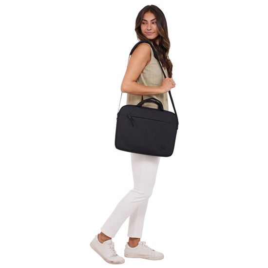 Una mujer camina llevando una bolsa negra para portátil. Viste top beige, pantalones blancos y zapatillas. El fondo es blanco.