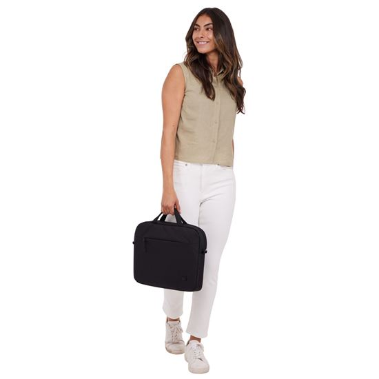 Una mujer con pantalones blancos y top beige lleva un maletín negro. Sonríe mientras mira a la izquierda. Fondo blanco.