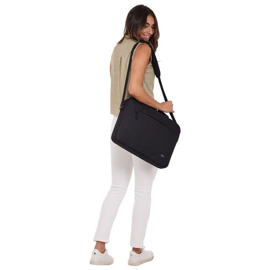 Mujer con top beige y pantalones blancos, llevando un bolso mensajero negro. Sonríe y mira por encima del hombro.