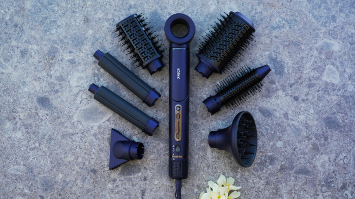 Un secador de pelo azul oscuro con accesorios, dispuestos sobre una superficie gris. Los accesorios incluyen cepillos, boquillas y herramientas de peinado.