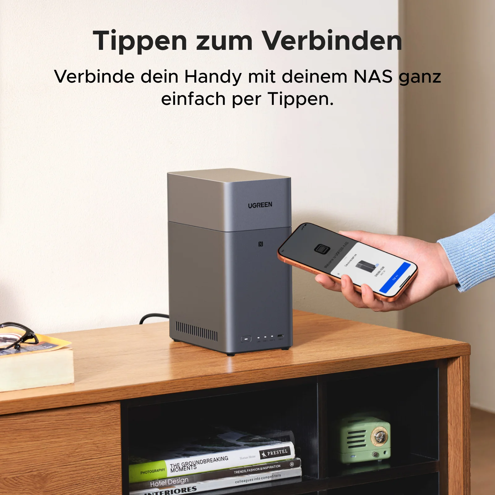 Eine Person hält ein Telefon in der Nähe eines UGREEN NAS-Servers. Der Telefonbildschirm zeigt die Einrichtung der Verbindung. Bücher und ein Radio stehen auf dem Regal.