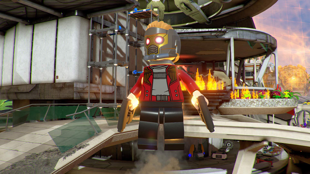 Lego Star-Lord con pistole a mezz'aria. Giacca rossa, pantaloni neri e casco d'oro. Fiamme ed edifici sullo sfondo.