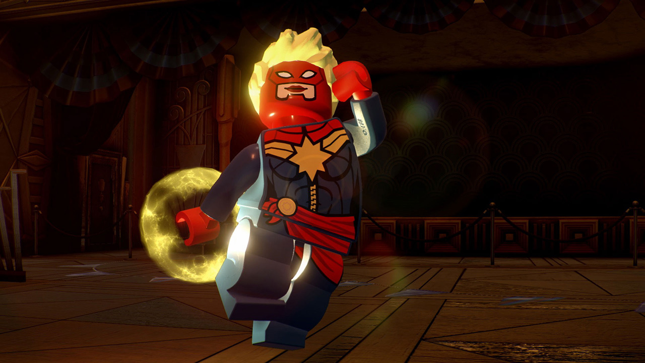 Lego Captain Marvel in una stanza. Indossa rosso e blu. Un globo giallo brillante è alla sua sinistra. Lo sfondo è debolmente illuminato.
