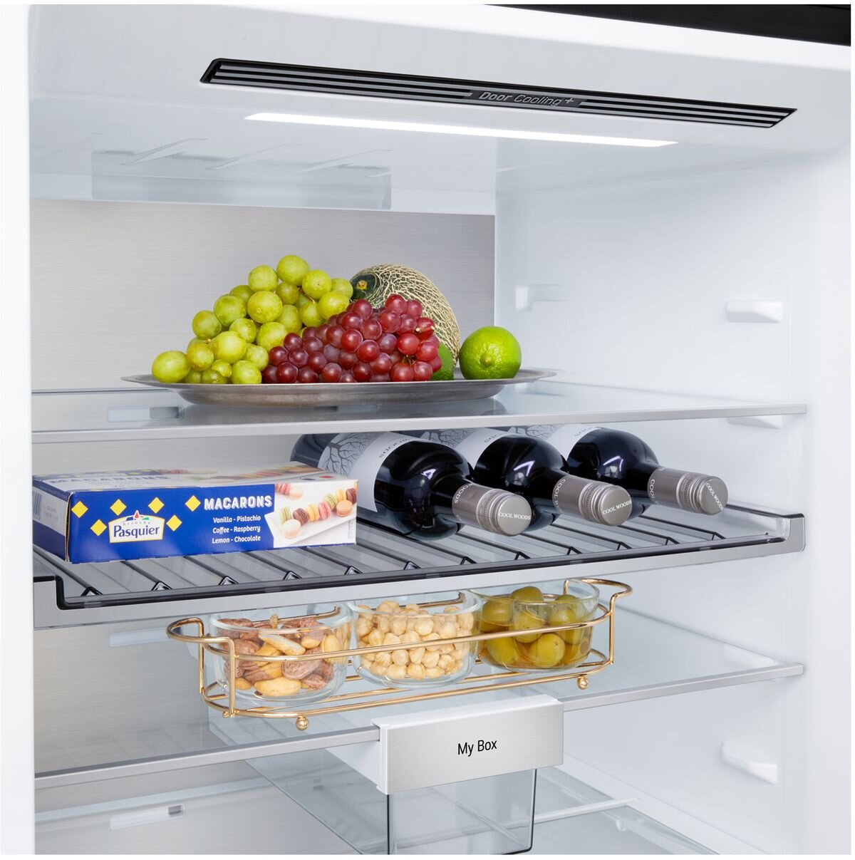 W lodówce widoczne są winogrona, melon i butelki wina. Przechowywane są również makaroniki, orzechy i oliwki.