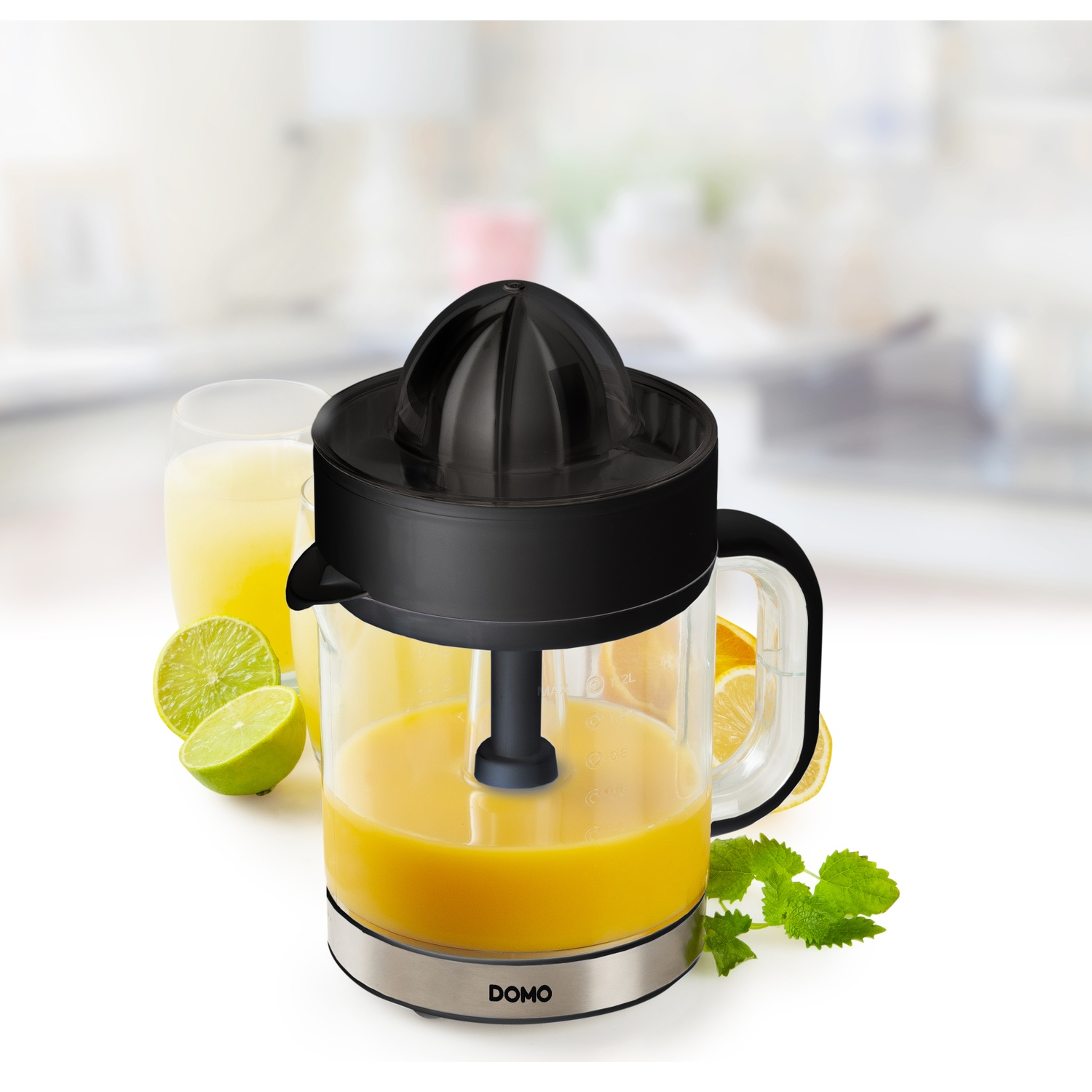 A juicer with orange juice, limes, and a glass of juice. It has a black top and a silver base. Mint leaves are on the side.