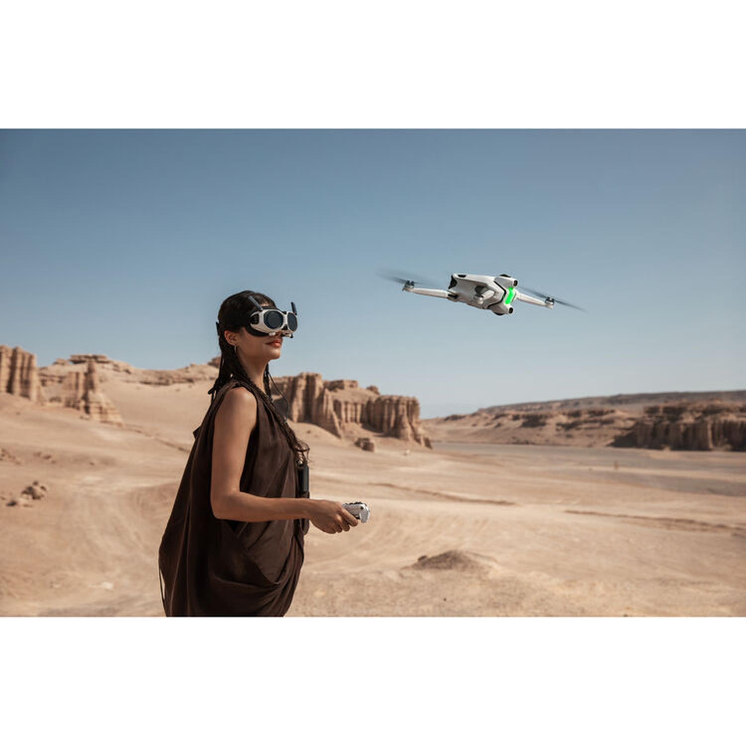 Een vrouw met een VR-bril en afstandsbediening bestuurt een drone in een woestijnlandschap onder een helderblauwe lucht.