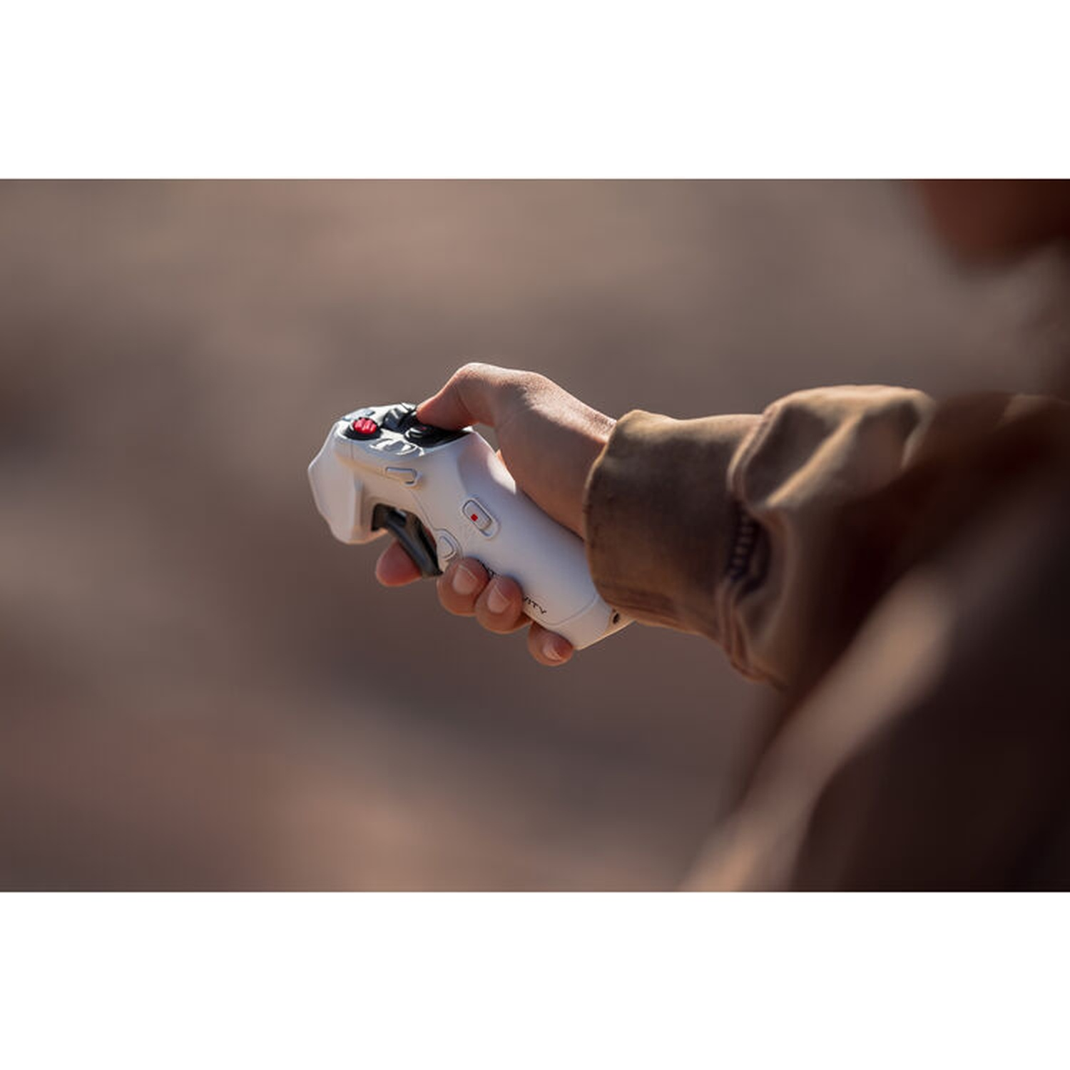 Een hand houdt een witte gamecontroller met rode knoppen vast. De achtergrond is wazig, met een bruine jas.
