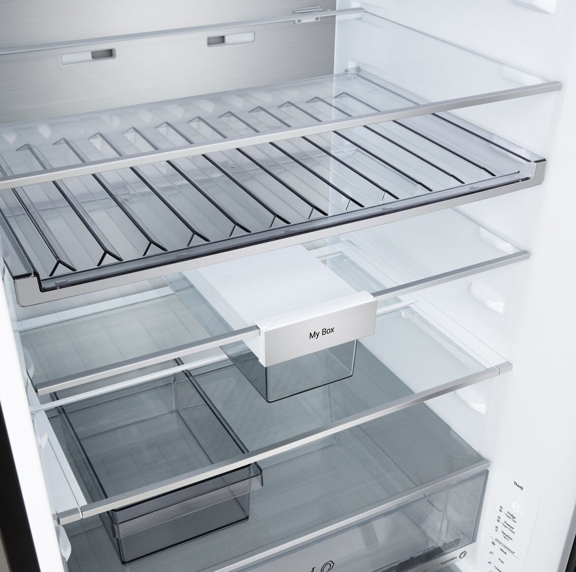 Wnętrze lodówki, widoczne półki, druciane kosze i szuflady. Białe pudełko z napisem 'My Box'. Wnętrze jest czyste i puste.