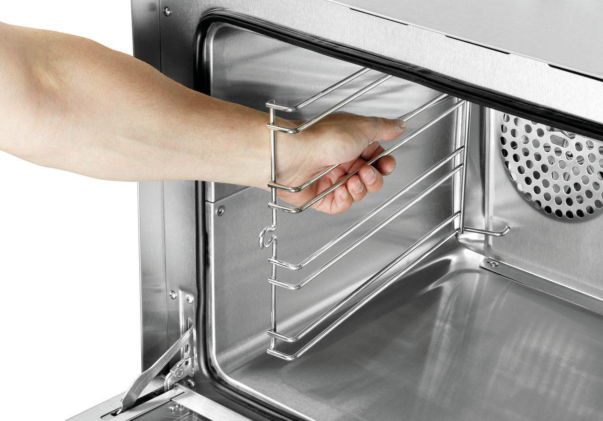 Eine Hand, die einen Ofenrost in einen Edelstahlbackofen einsetzt. Der Ofen ist offen und gibt den Innenraum und die Schienen frei.