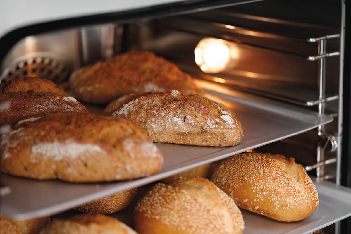 Mehrere Brotlaibe backen im Ofen. Die Laibe sind goldbraun, einige haben Sesamsamen.