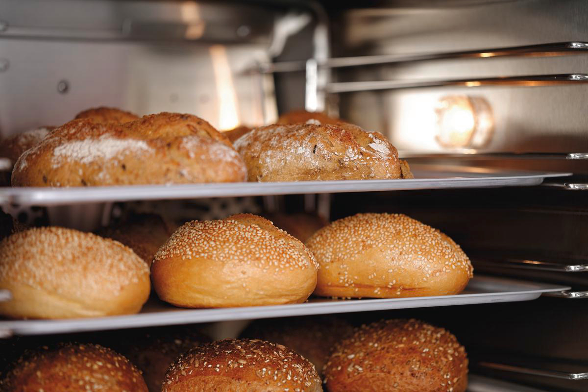 In einem Ofen sind verschiedene Brotlaibe und Brötchen auf Regalen angeordnet. Das Brot ist goldbraun, manche mit Sesamkörnern.