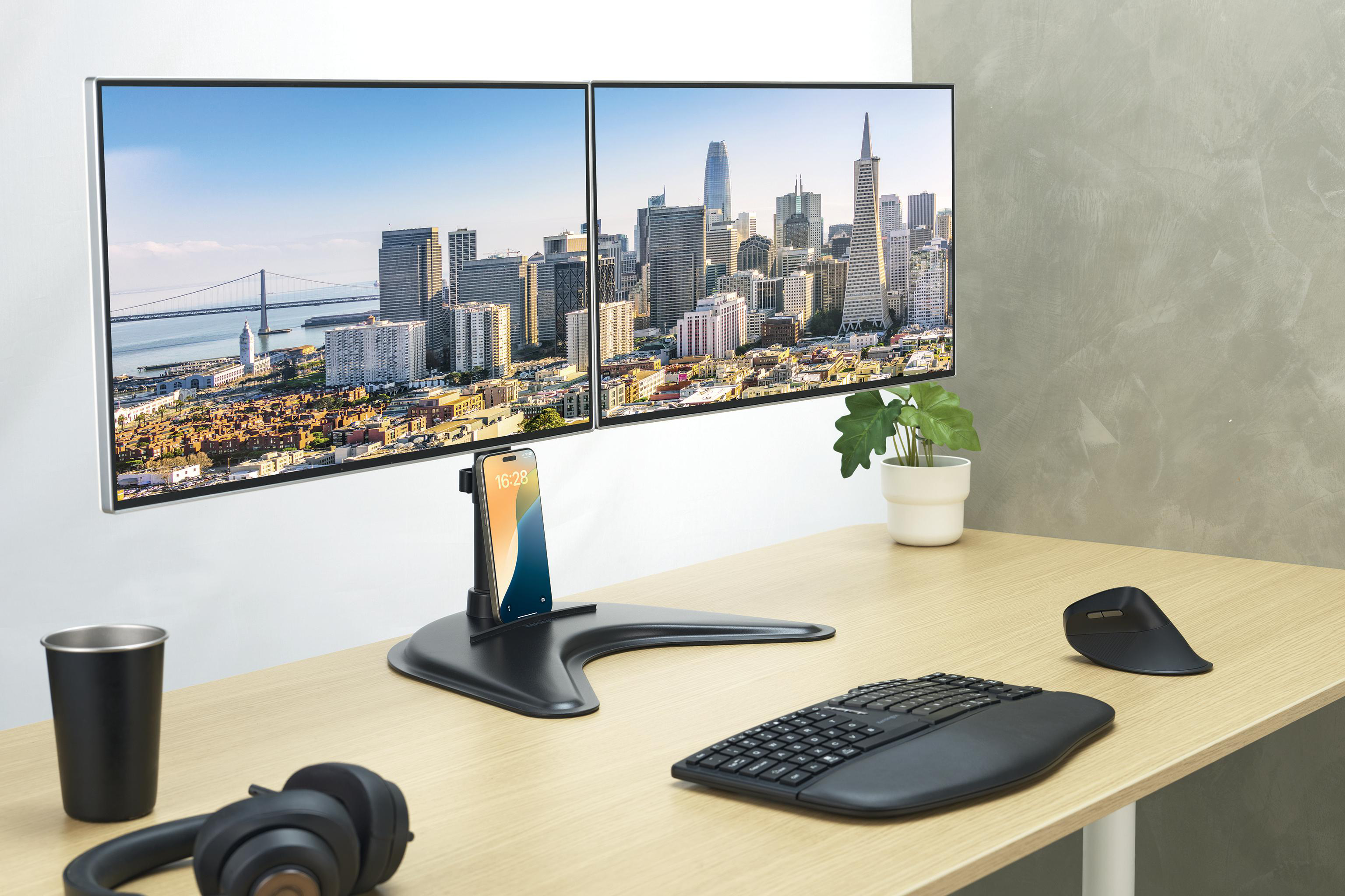 Schreibtisch mit zwei Monitoren, die San Francisco zeigen. Telefonständer, Tastatur, Maus, Kopfhörer und Pflanze sind ebenfalls vorhanden.