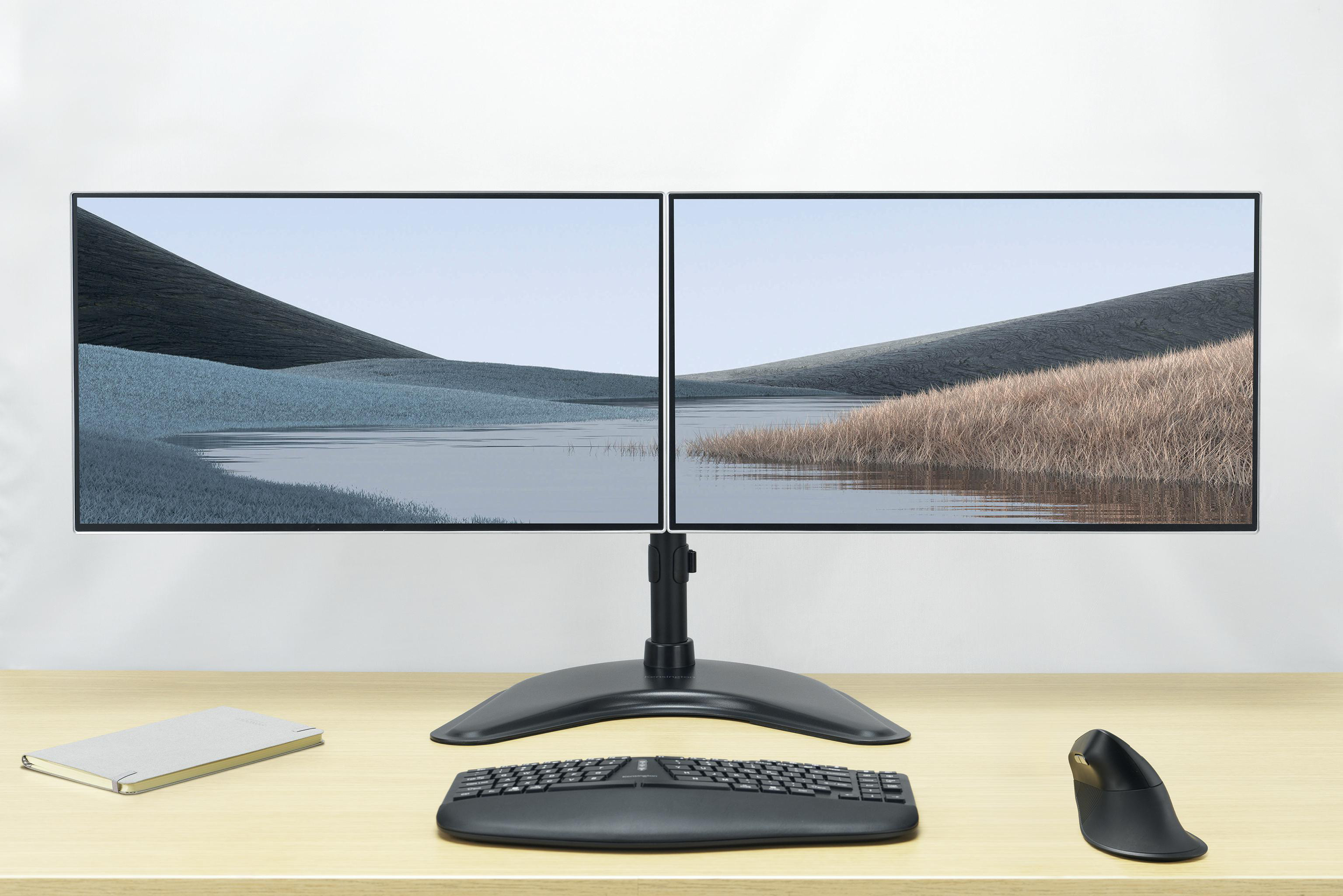 Zwei Monitore zeigen eine Landschaft. Tastatur, Maus und Notizbuch auf einem Holztisch.