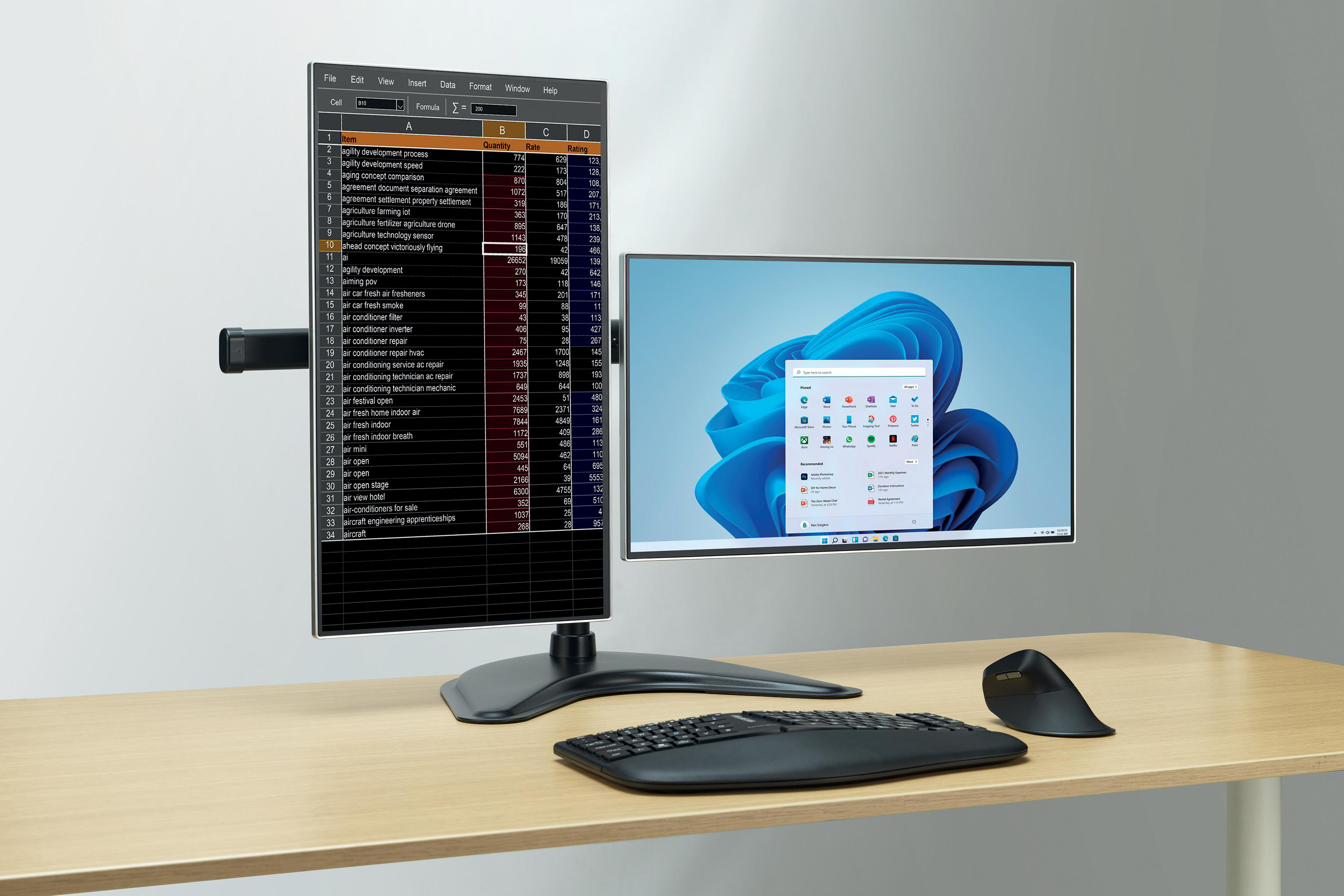 Schreibtisch-Setup mit zwei Monitoren, Tastatur, Maus und einer geöffneten Tabelle mit Daten.