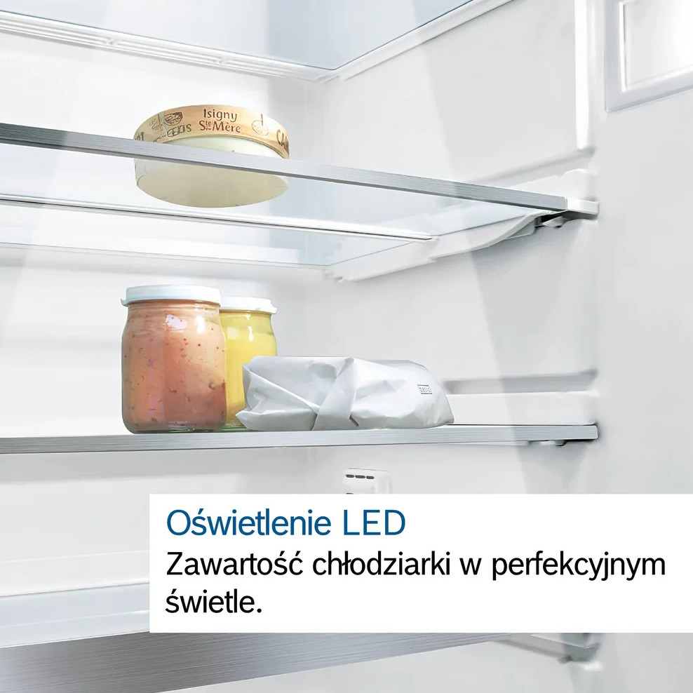 Wewnątrz lodówki: ser, słoiki i opakowanie na półkach, oświetlone światłem LED. Lodówka jest czysta i biała.