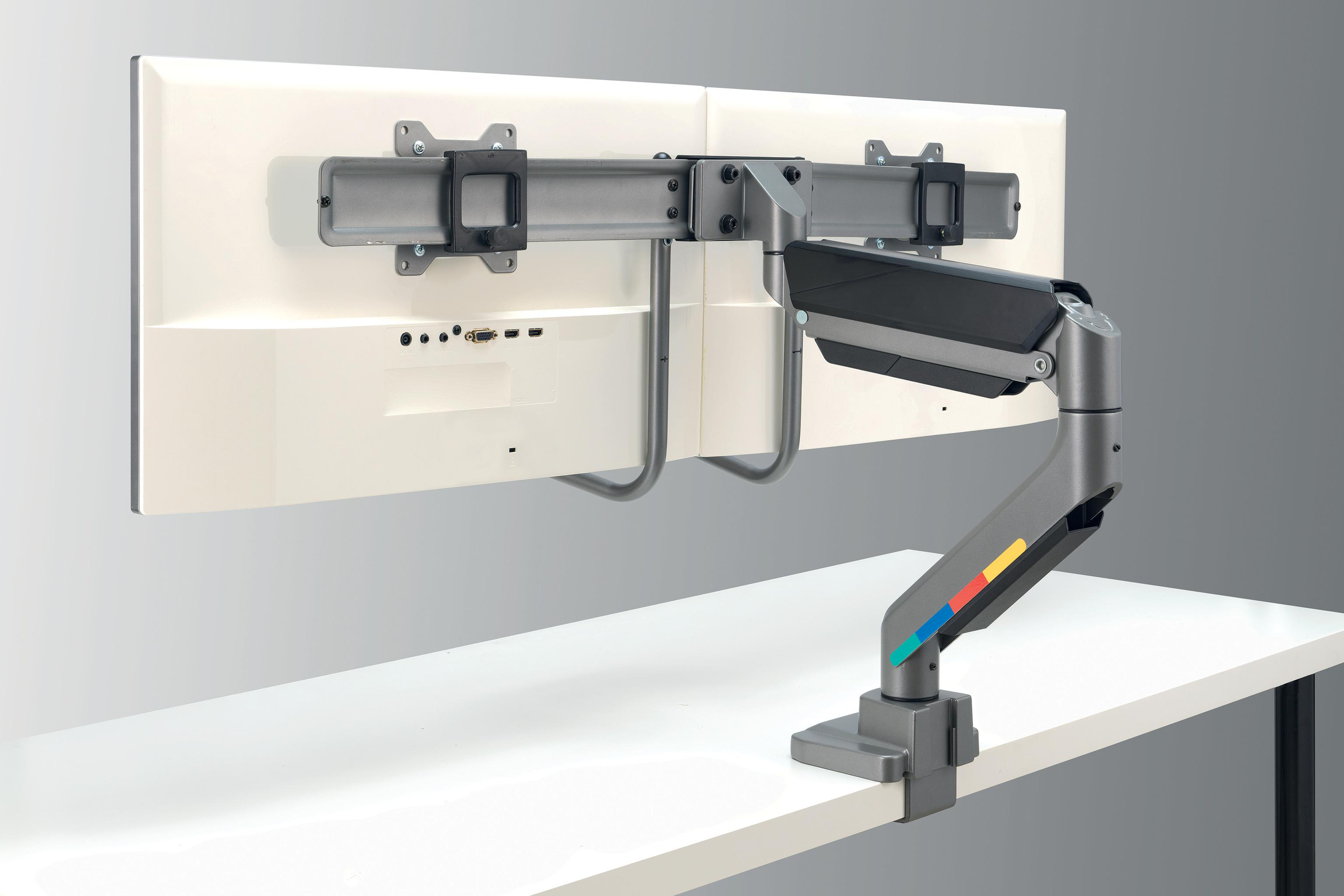Monitorarm mit zwei Monitoren. Grauer Arm mit farbigen Streifen auf weißem Schreibtisch, grauer Hintergrund.