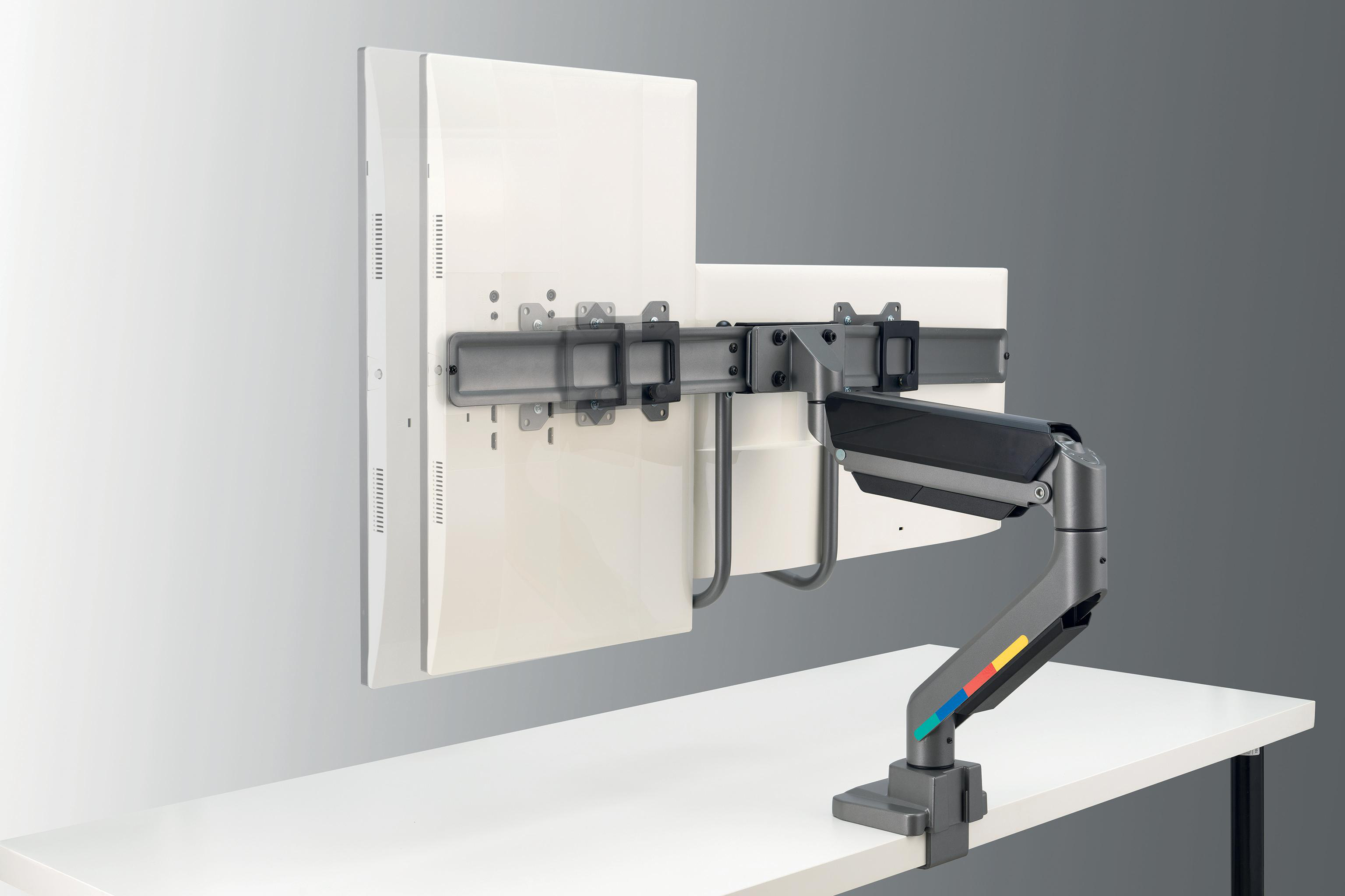 Monitorarm mit zwei Monitoren. Der Arm ist grau mit farbigen Streifen, montiert auf einem weißen Schreibtisch.