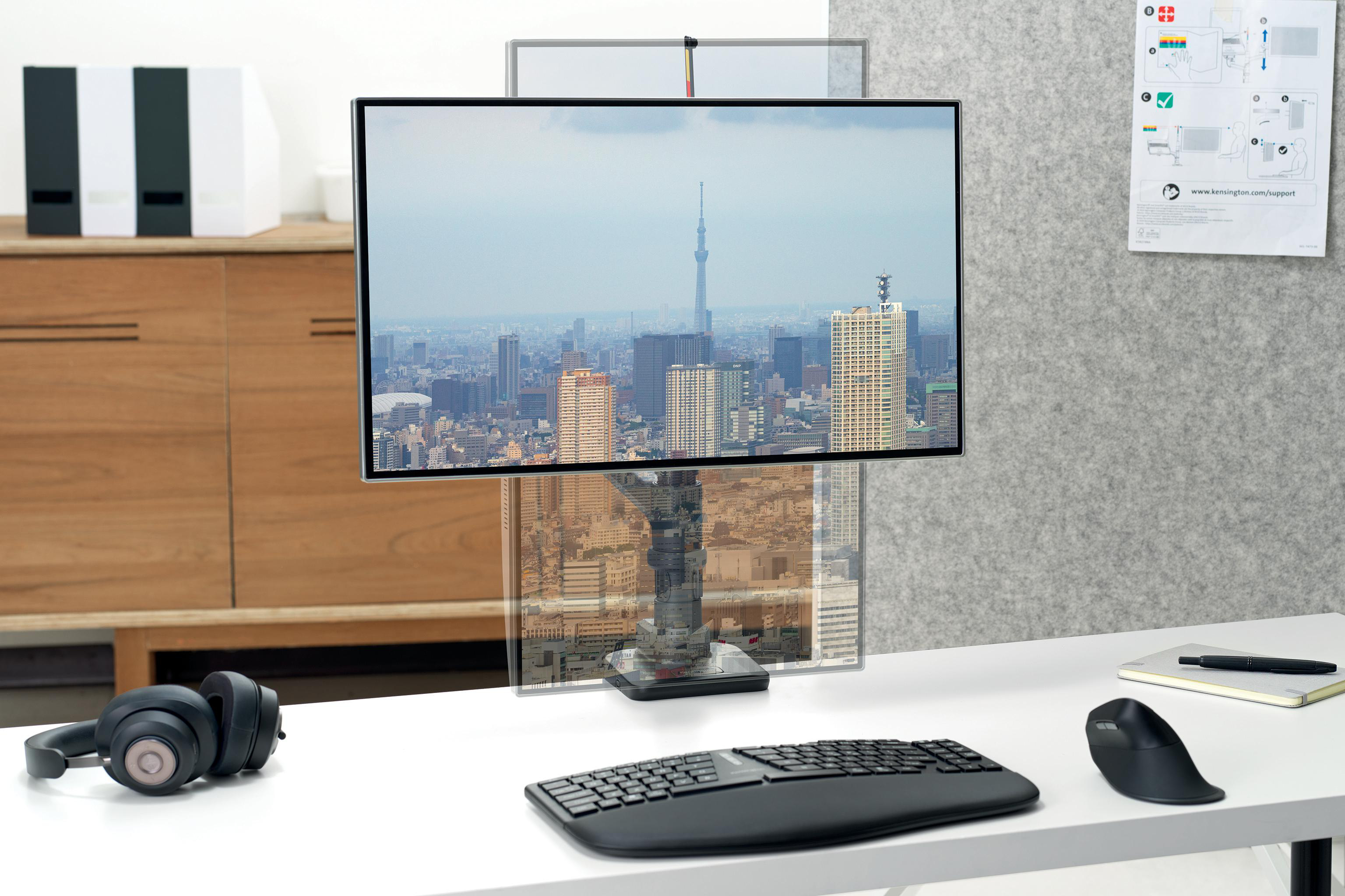 Ein Computermonitor zeigt eine Stadtlandschaft. Tastatur, Maus und Kopfhörer liegen auf einem weißen Schreibtisch.
