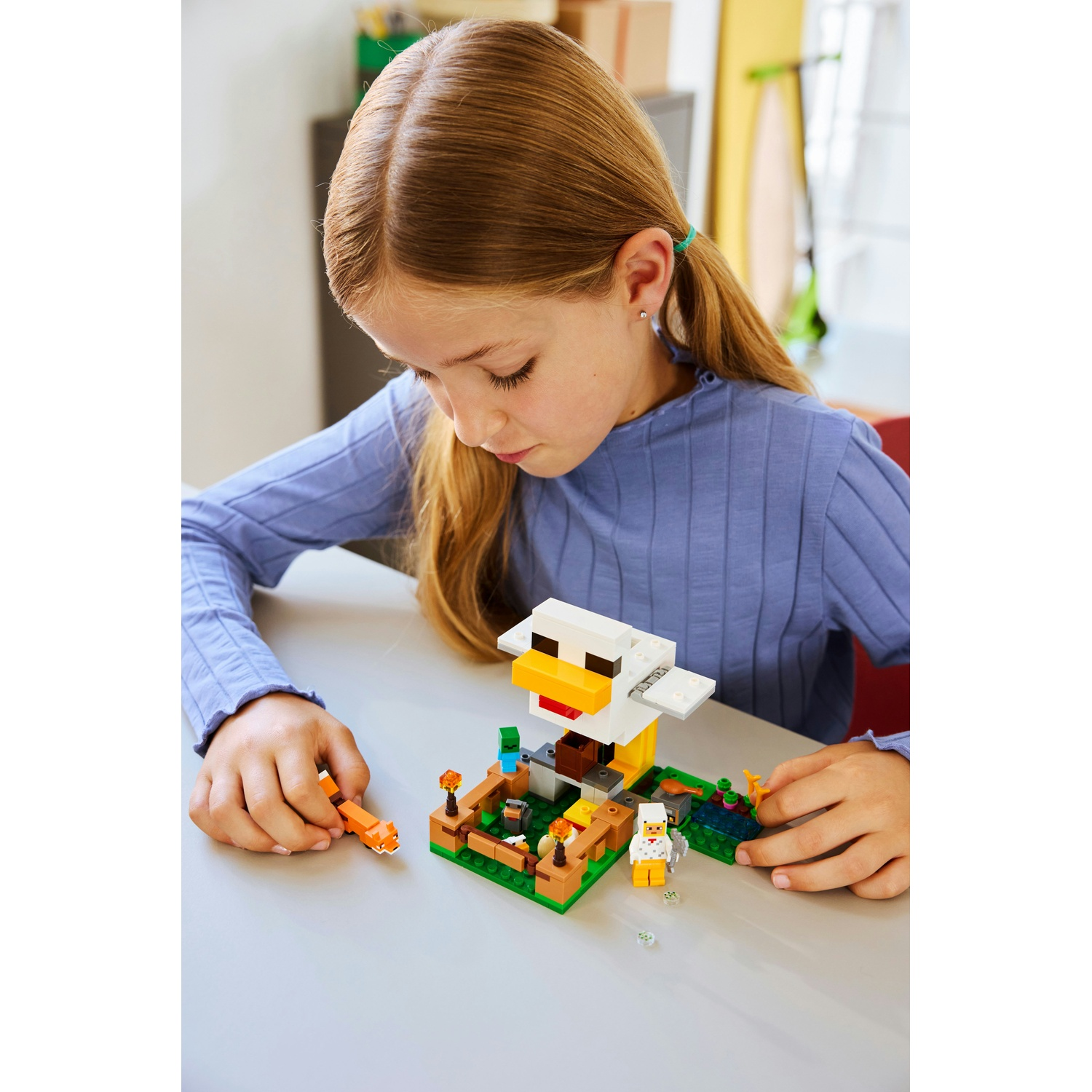 Una ragazza gioca con un set Lego di Minecraft. Il set presenta una casa per polli e piccole figure. La ragazza è concentrata sul gioco.