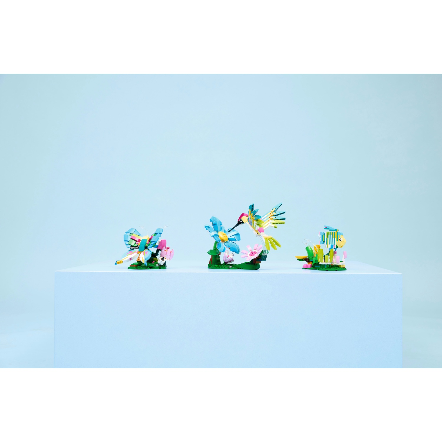 Tre colorati modelli Lego di uccelli e fiori su una superficie bianca, sfondo blu, ognuno con design diversi.