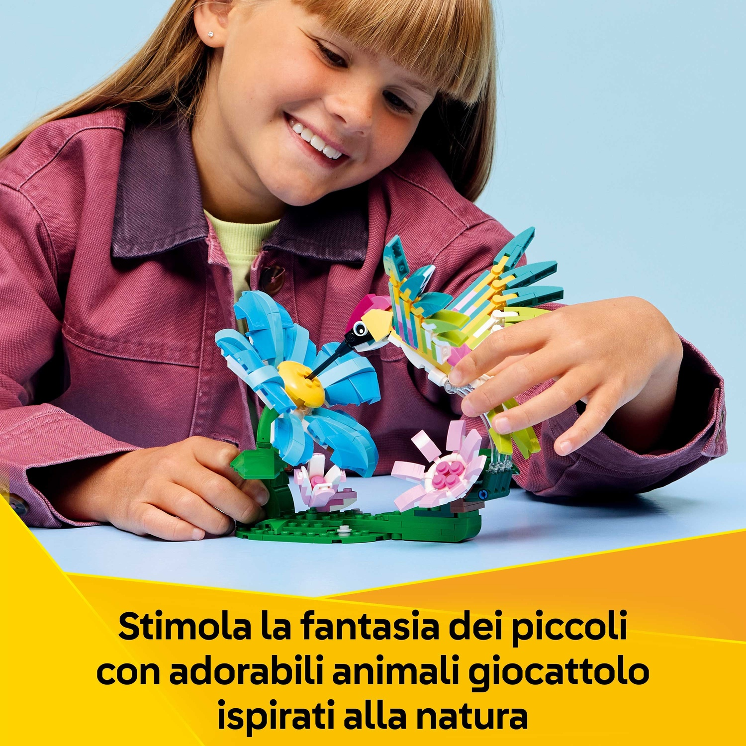 Una ragazza sorride a un set LEGO di fiori e uccelli. Il set comprende fiori blu, fiori rosa e un uccello colorato.